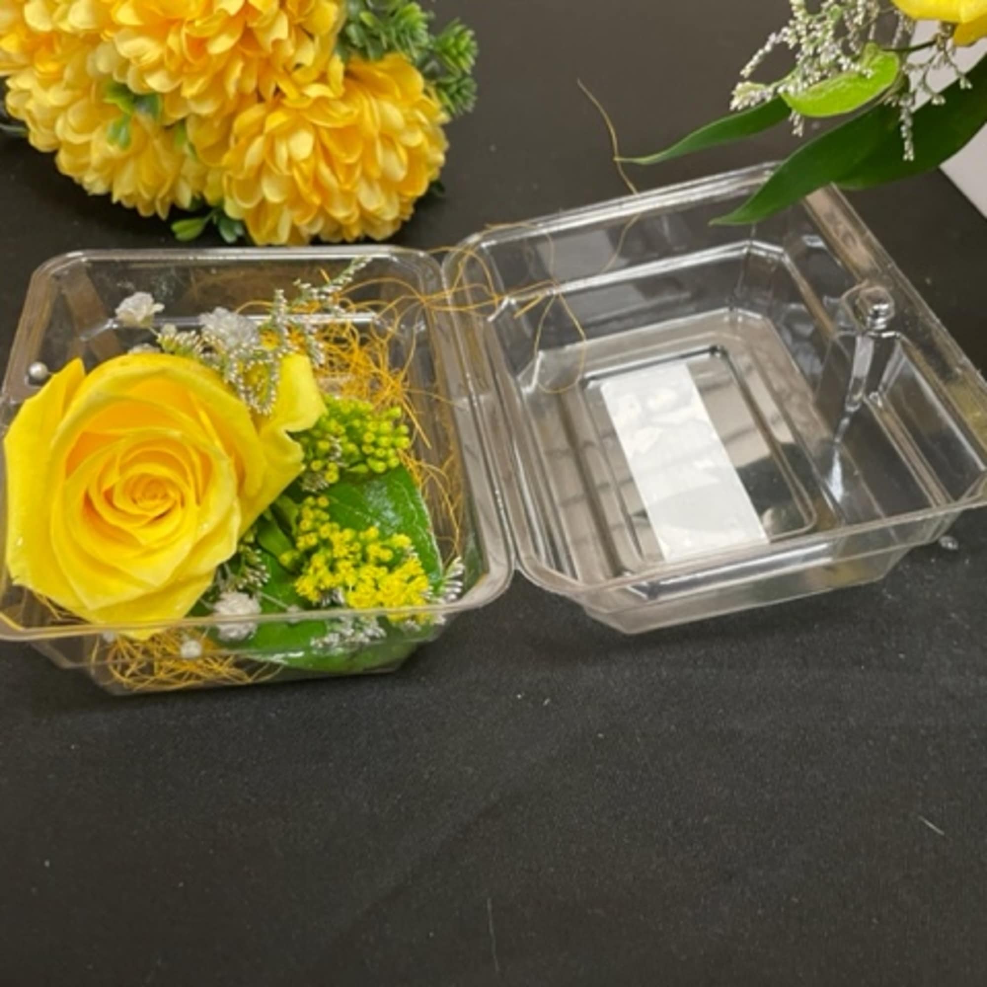 Yellow rose in a clear plastic box with small filler flowers