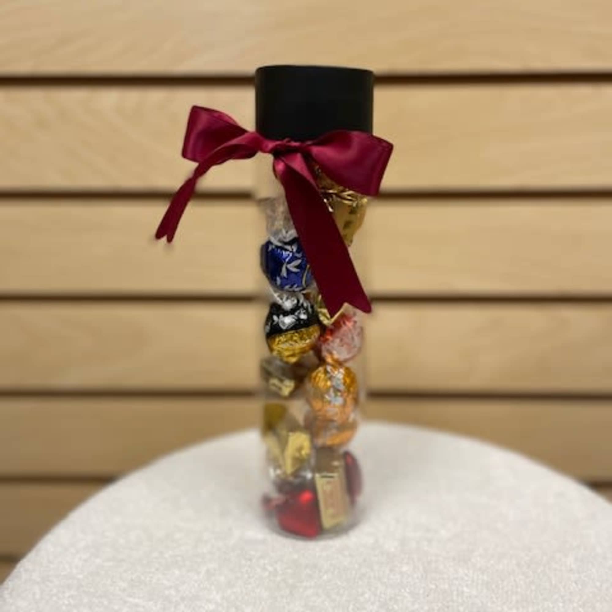 Clear tube filled with assorted wrapped chocolates and topped with a burgundy ribbon