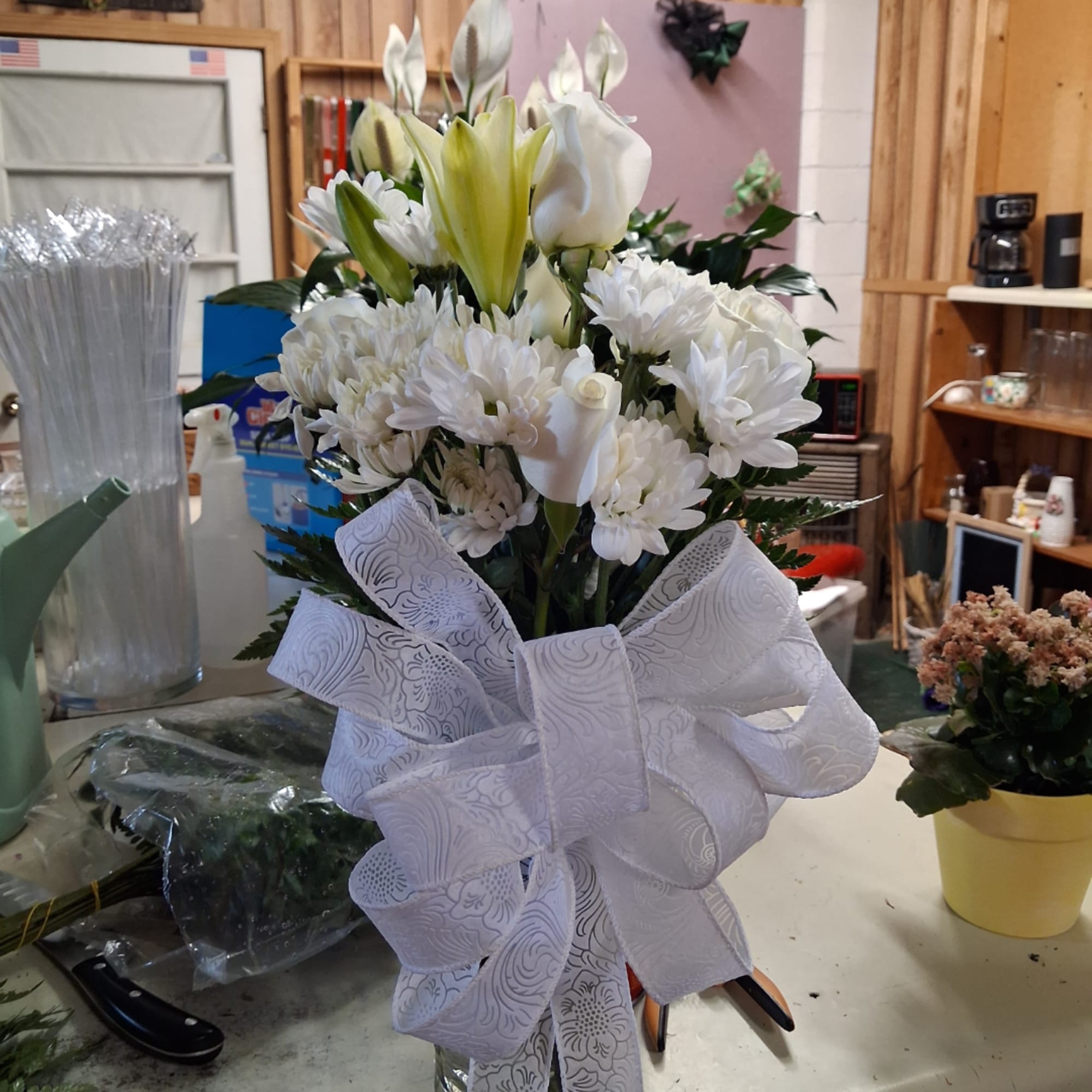 White floral arrangement with lilies and daisies tied with a large white bow