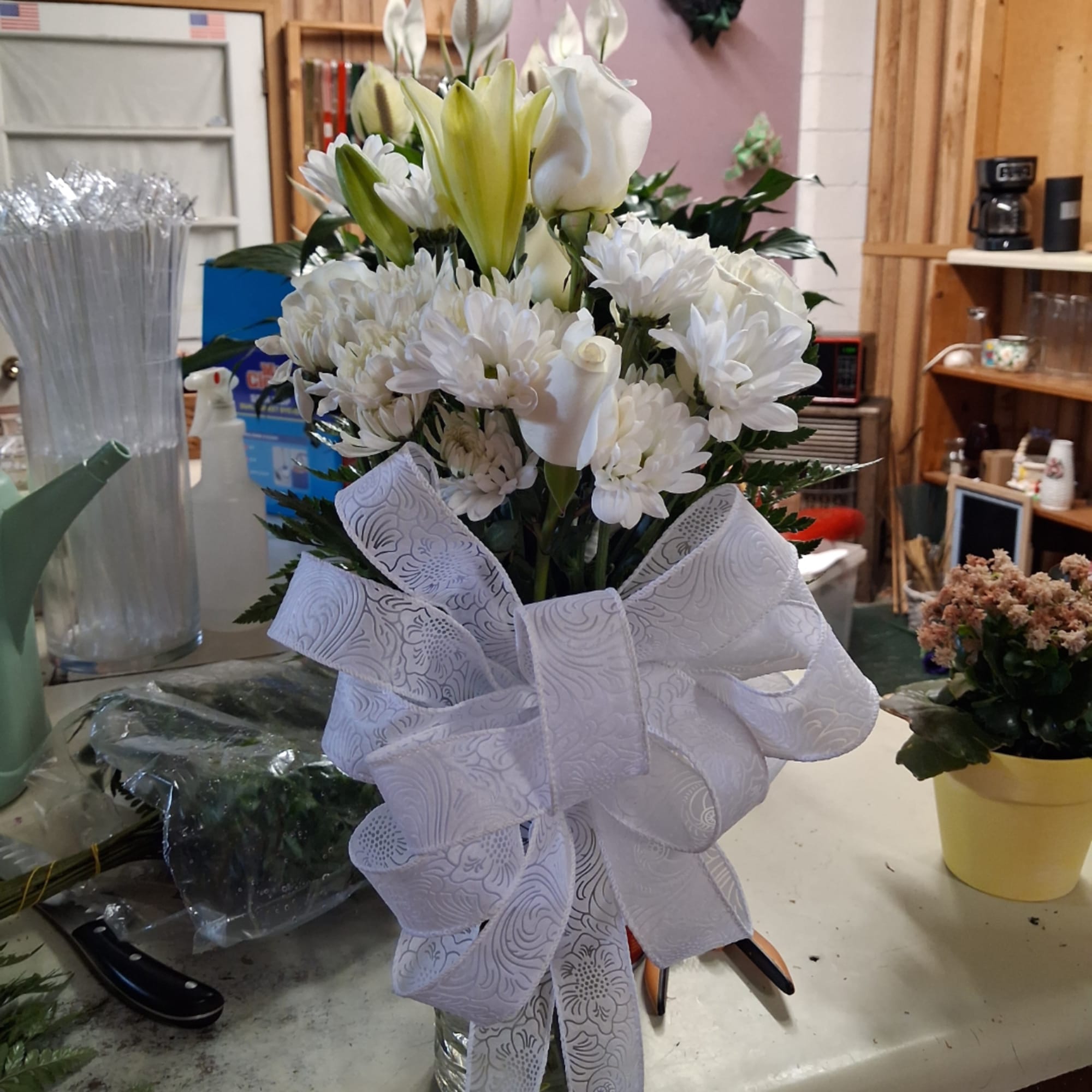 White lilies and daisies in a glass vase with a large white bow