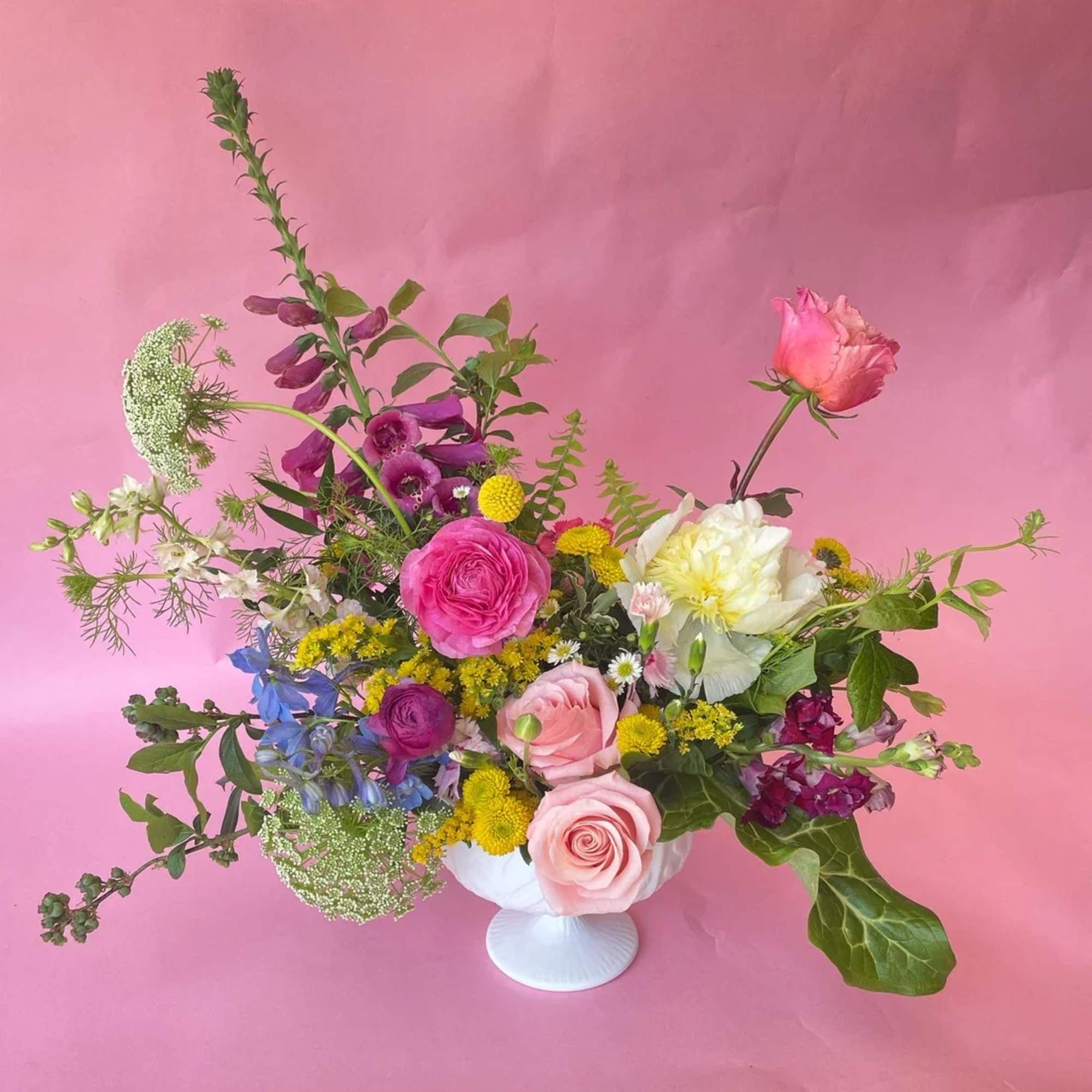 Mixed bouquet of pink, purple, yellow, and white flowers in a white vase