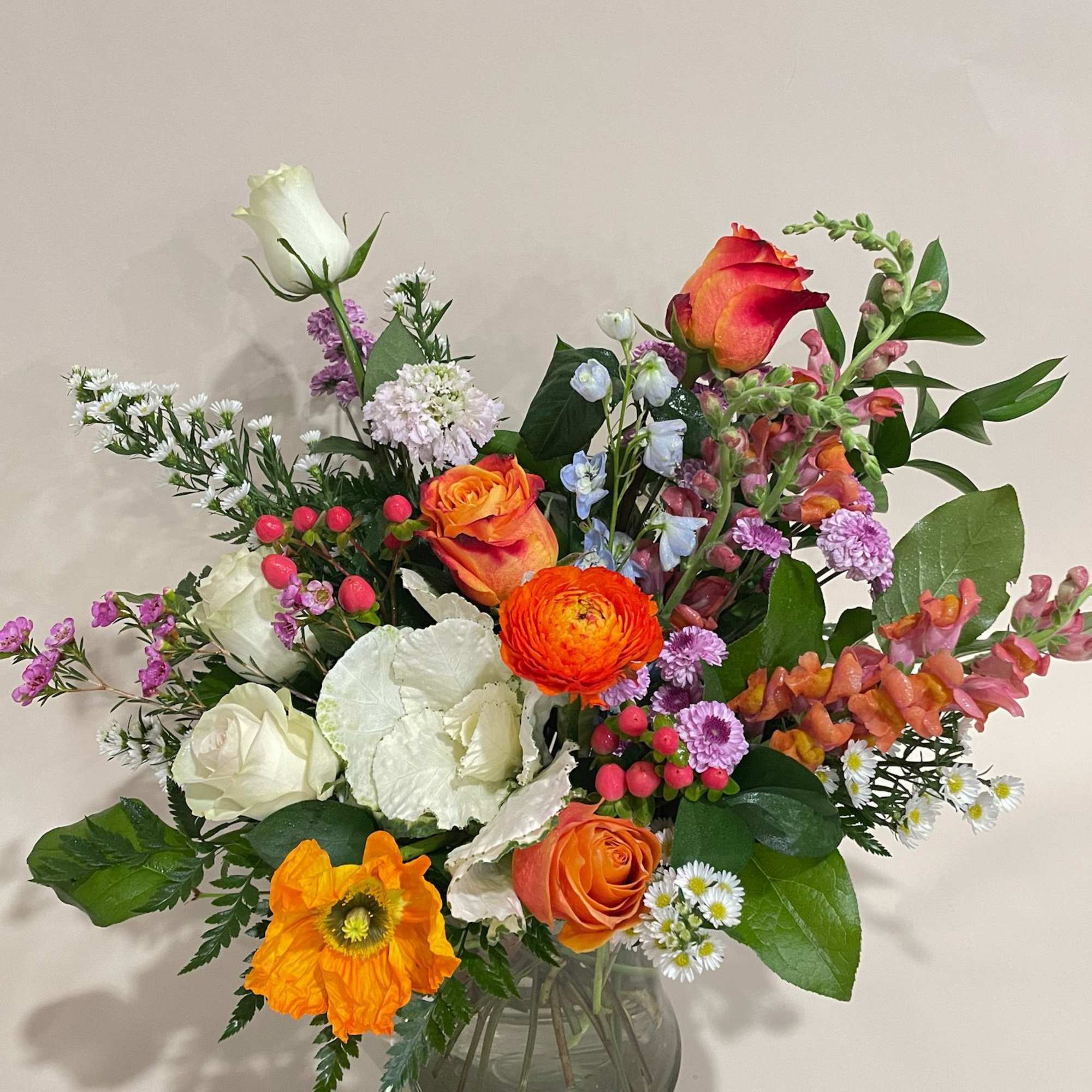 Mixed bouquet of orange, white, pink, and purple flowers in a glass vase