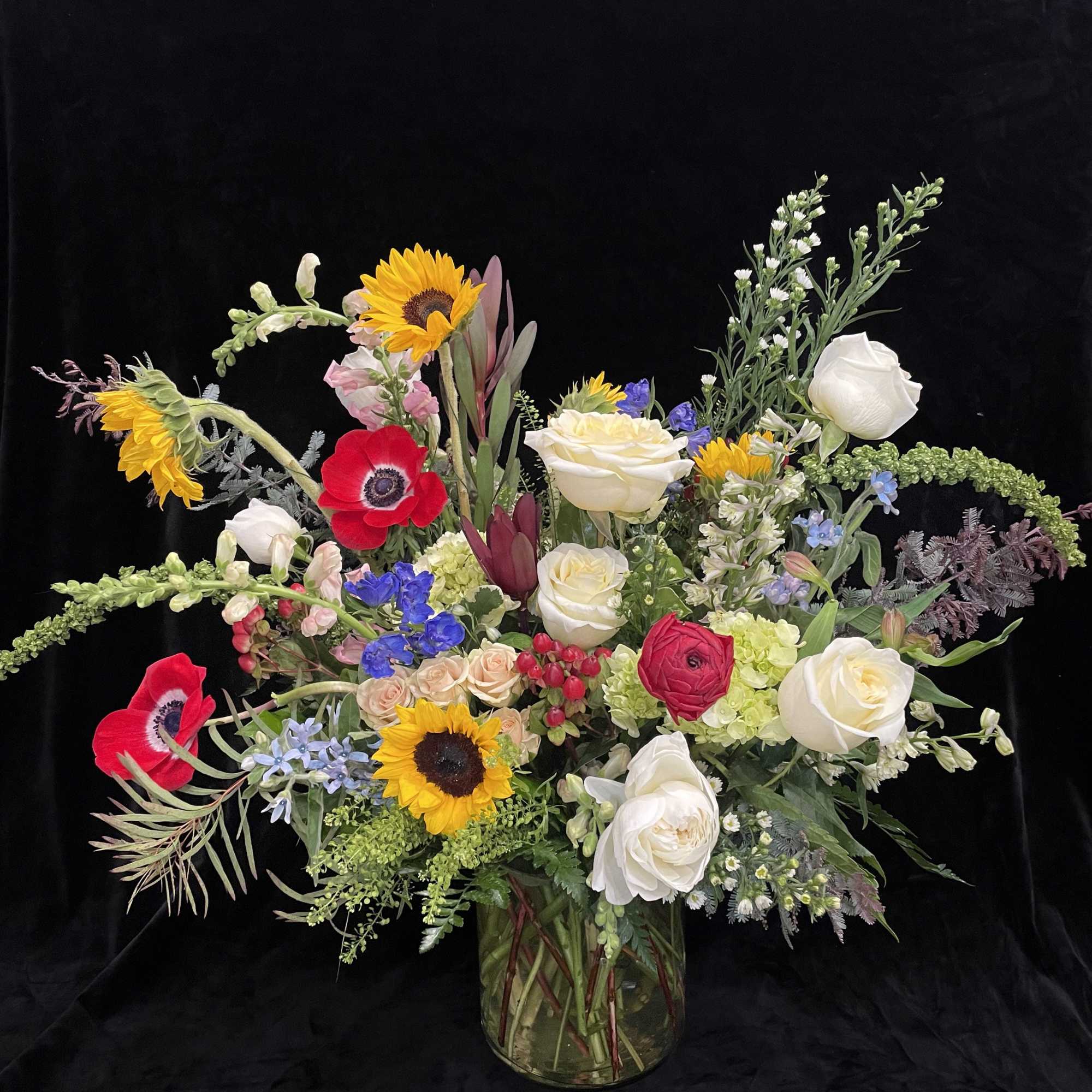 Mixed bouquet of sunflowers, roses, and anemones in a glass vase