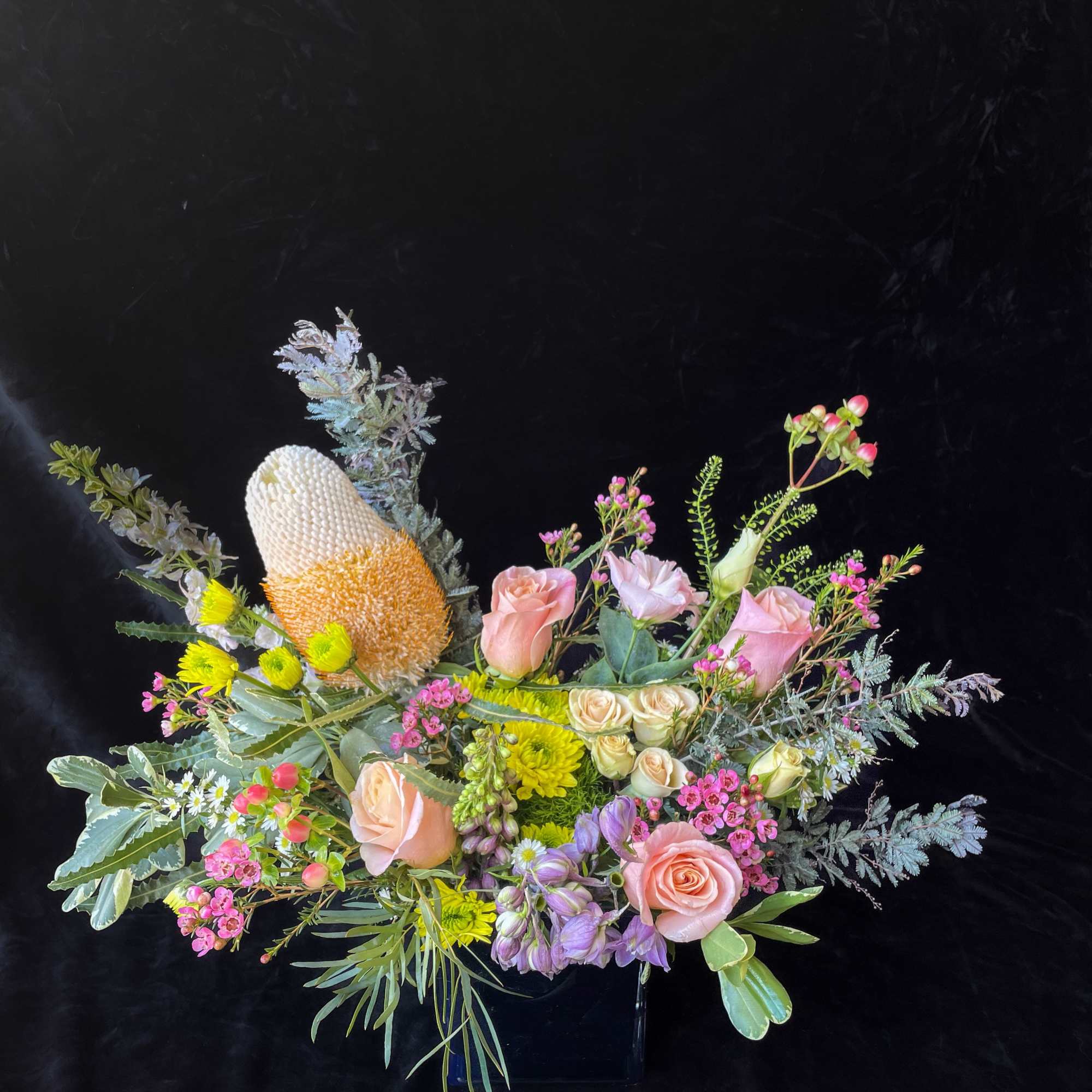 Mixed bouquet with pink roses, yellow blooms, and a large protea in a vase