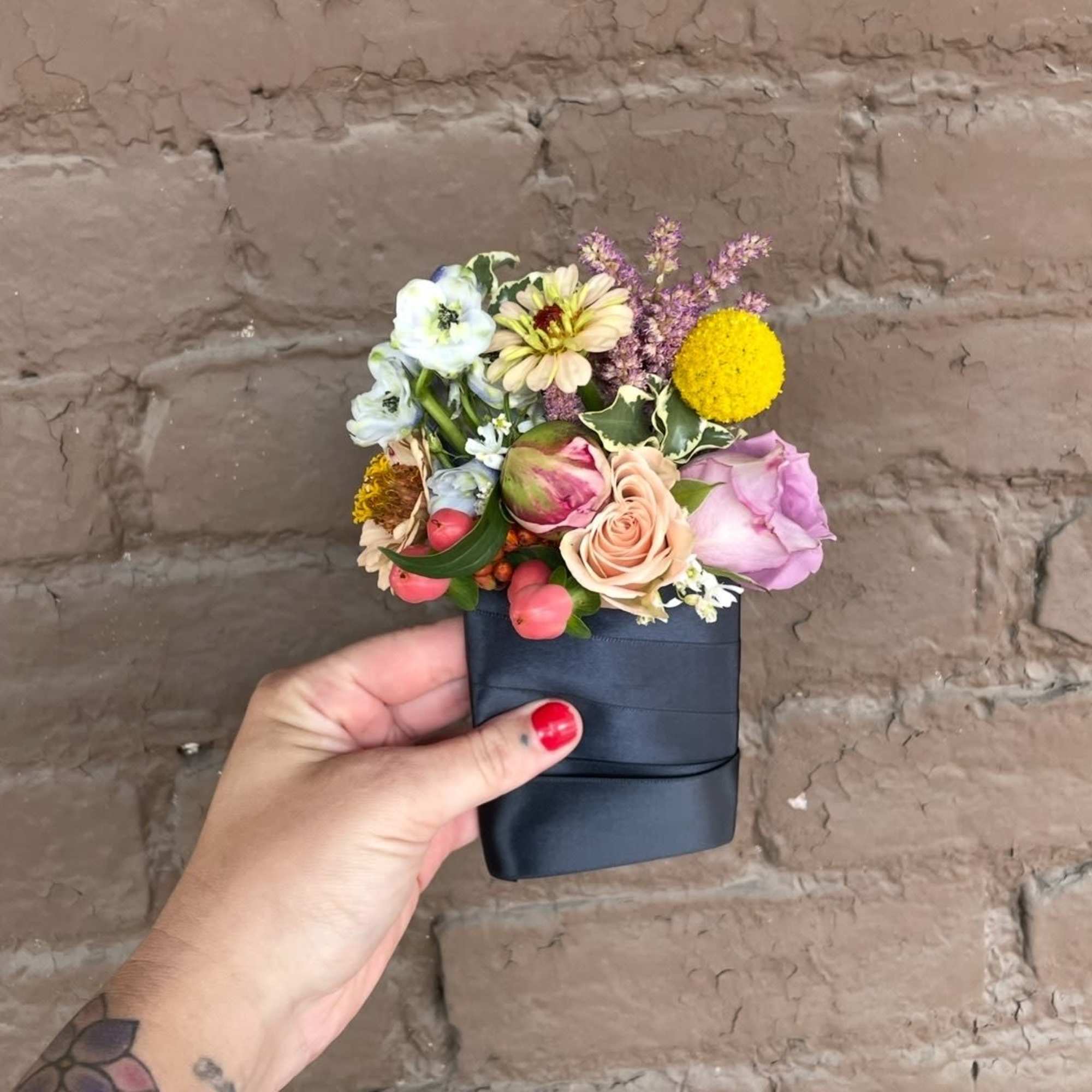 Small hand-held bouquet with mixed pastel flowers in a dark wrap
