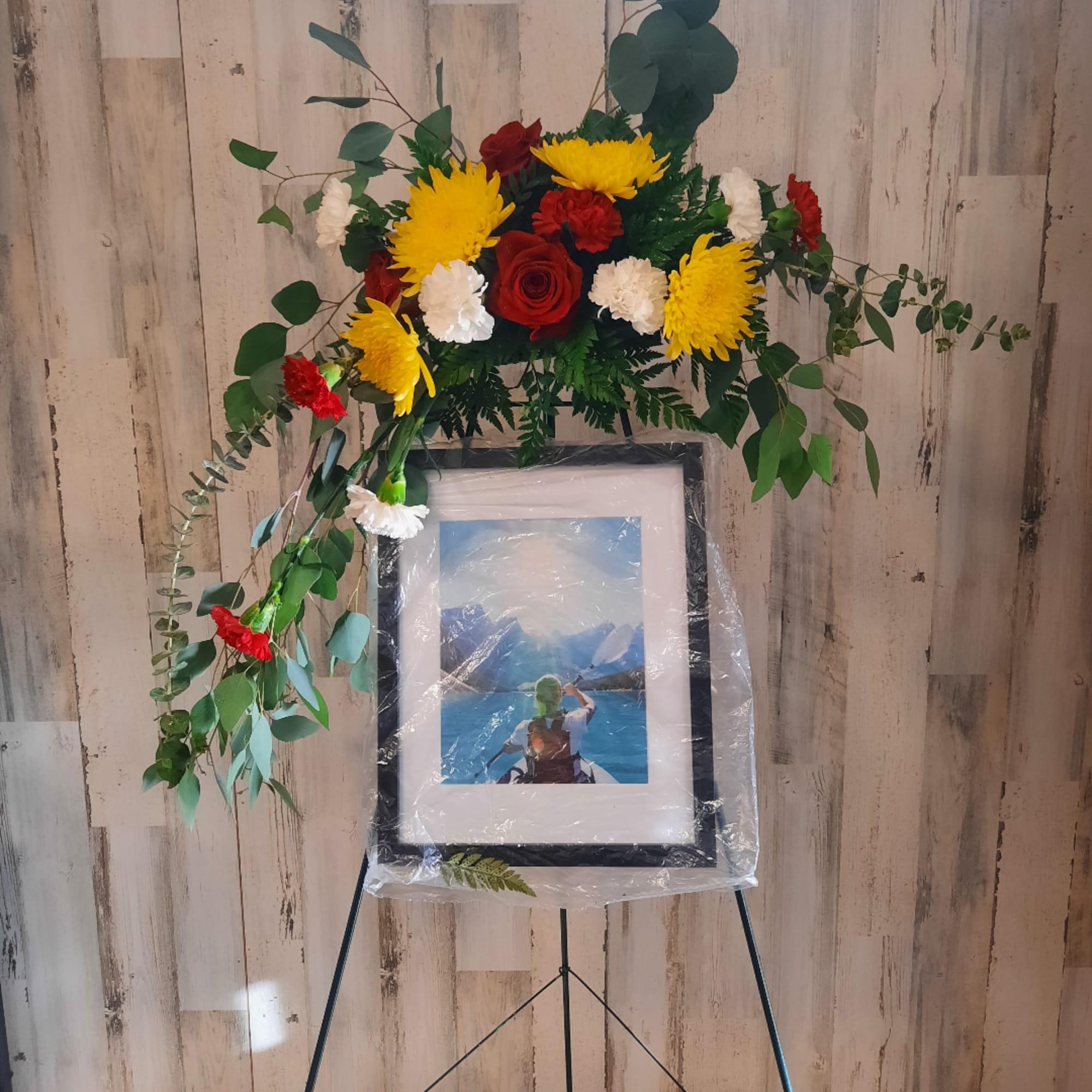 Floral standing spray with red, yellow, and white flowers on an easel