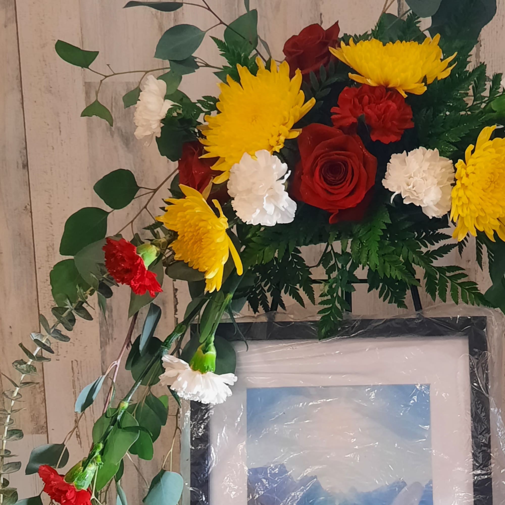 Red roses with yellow and white chrysanthemums arranged around a framed picture