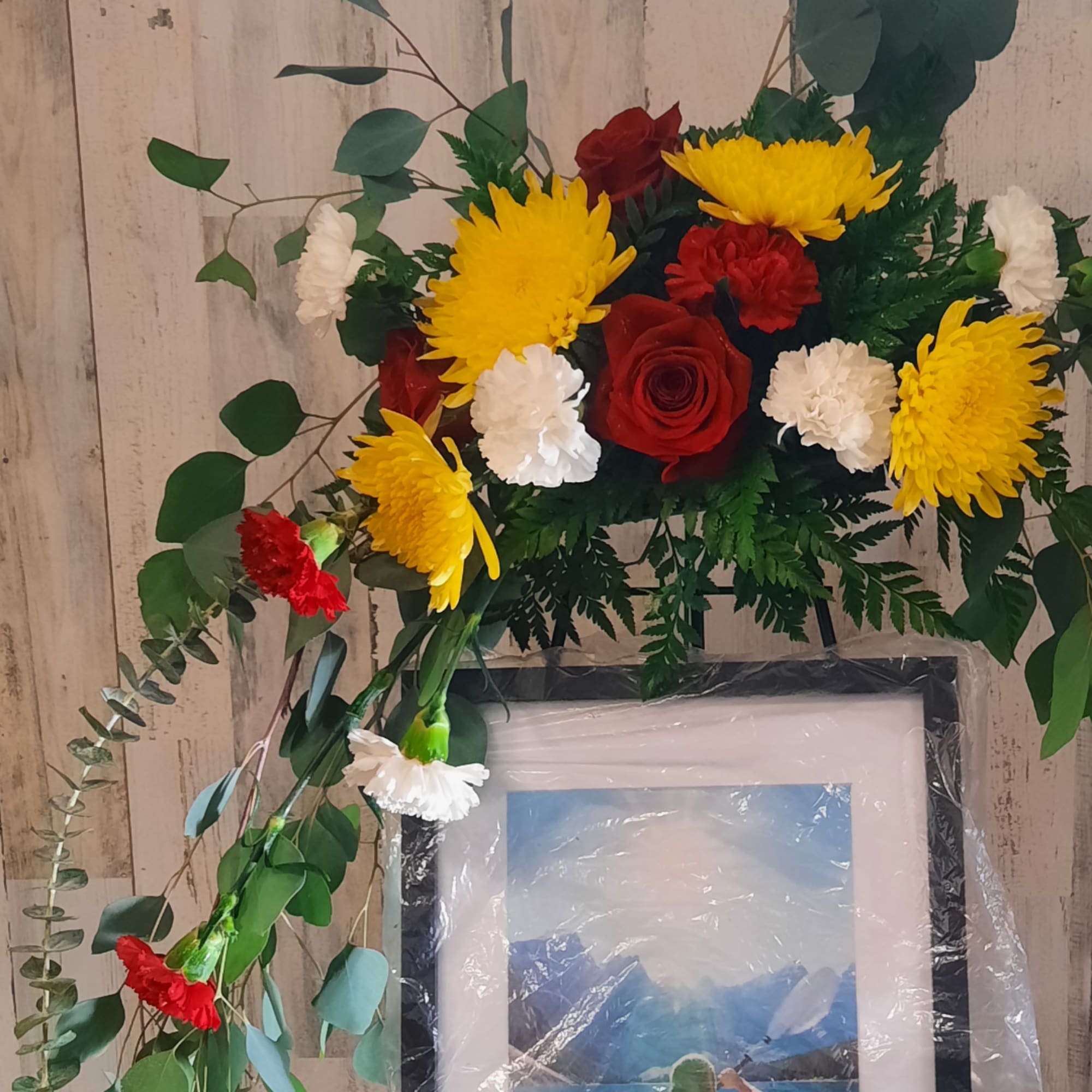 Red roses, yellow chrysanthemums, and white carnations in a framed floral display