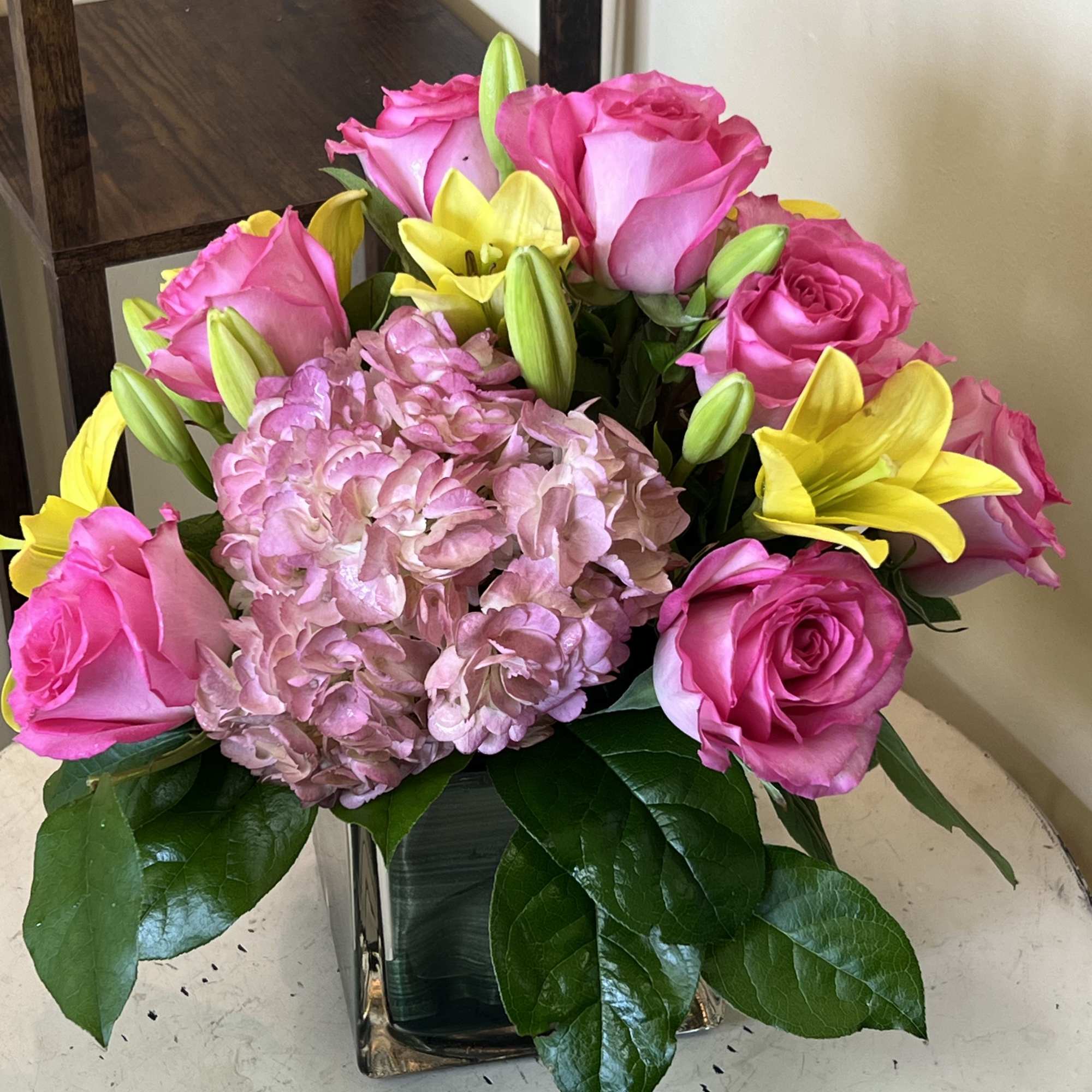 Pink roses and yellow lilies arranged with pale pink hydrangea in a glass vase