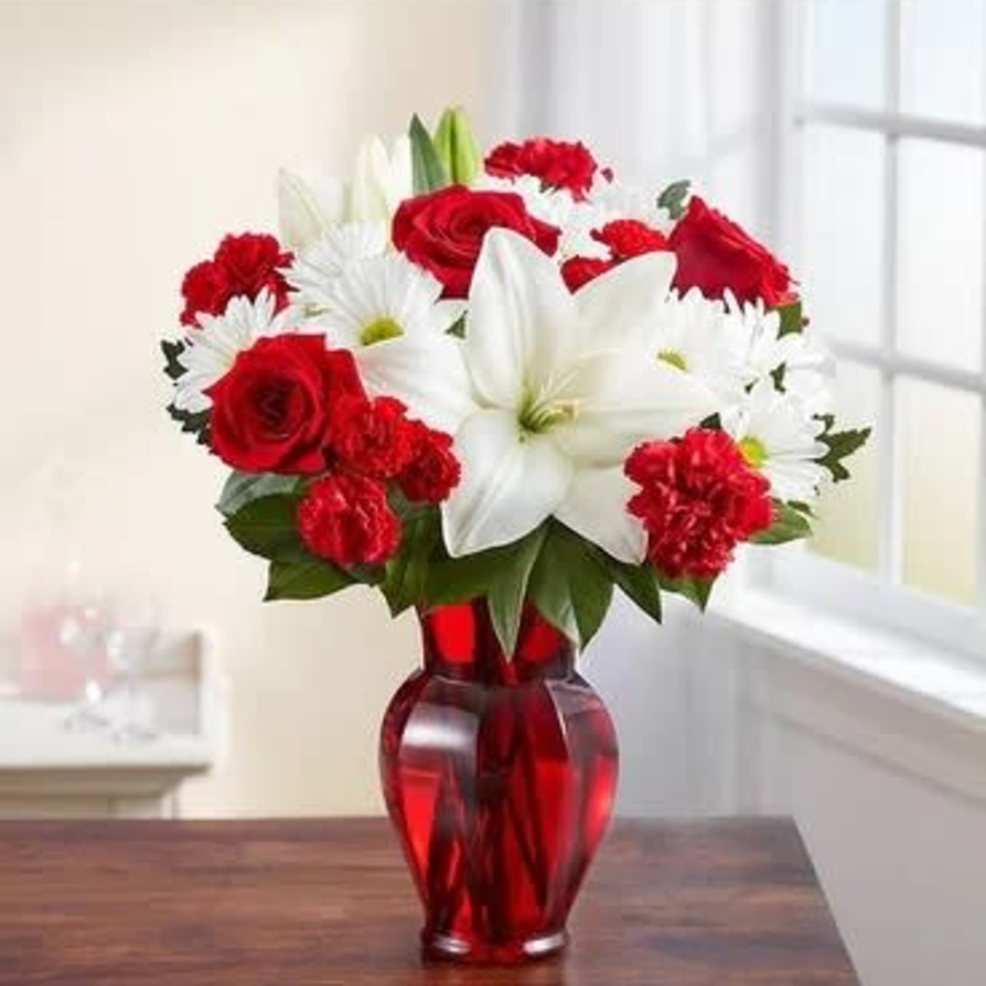 Red roses, white lilies, and white daisies in a red glass vase