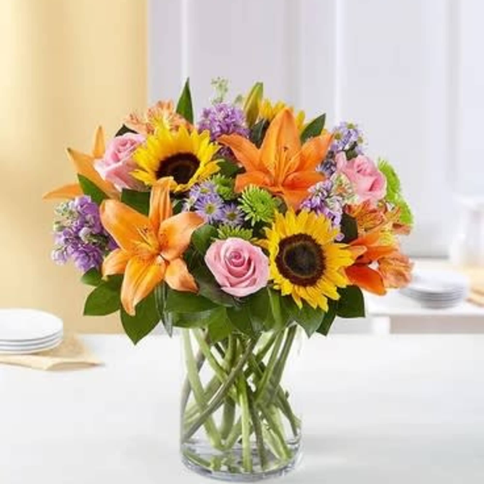 Mixed bouquet of sunflowers, lilies, and pink roses in a glass vase