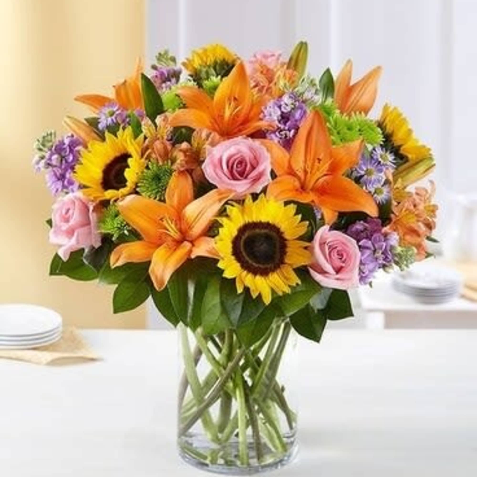 Bouquet of orange lilies, sunflowers, and pink roses in a glass vase