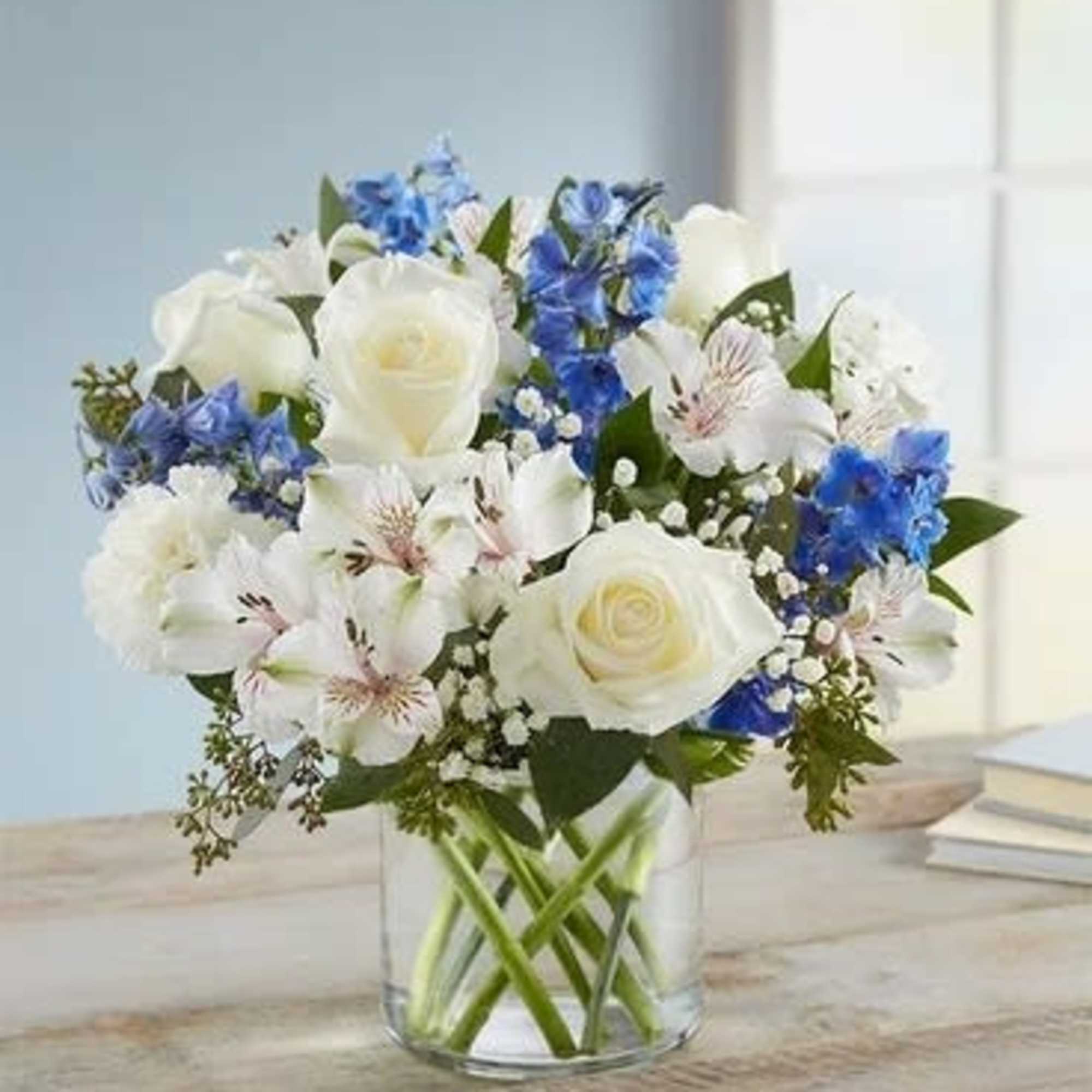 White roses and blue flowers arranged in a clear glass vase