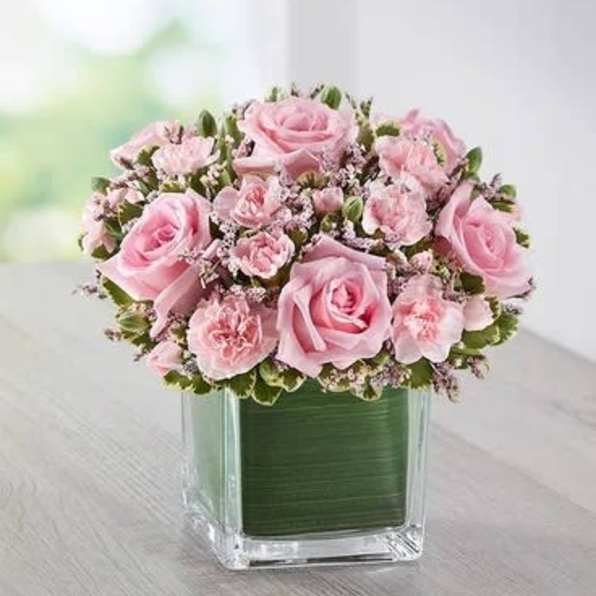 Pink roses and carnations arranged in a square glass vase
