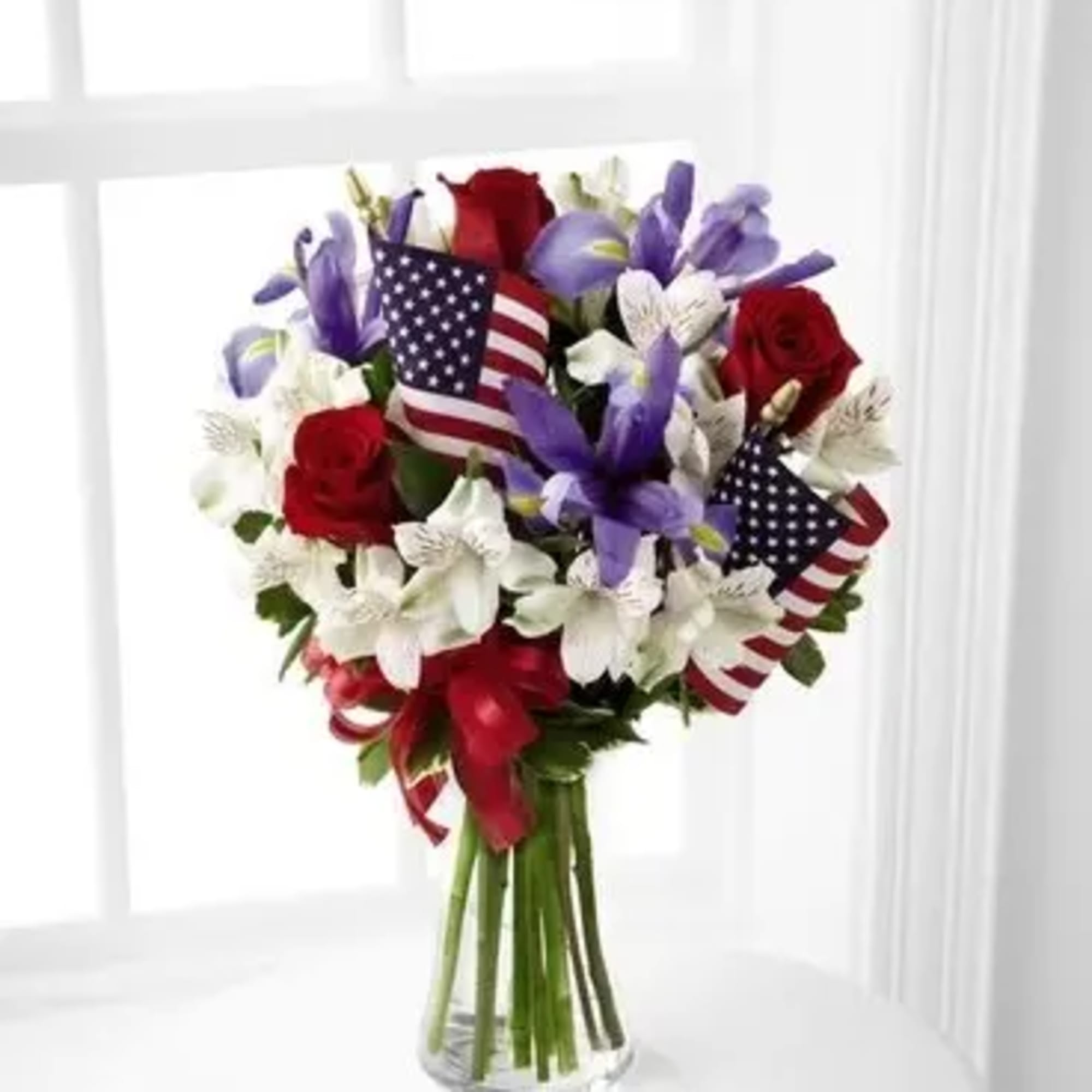 Bouquet of red, white, and purple flowers in a glass vase with small American flags