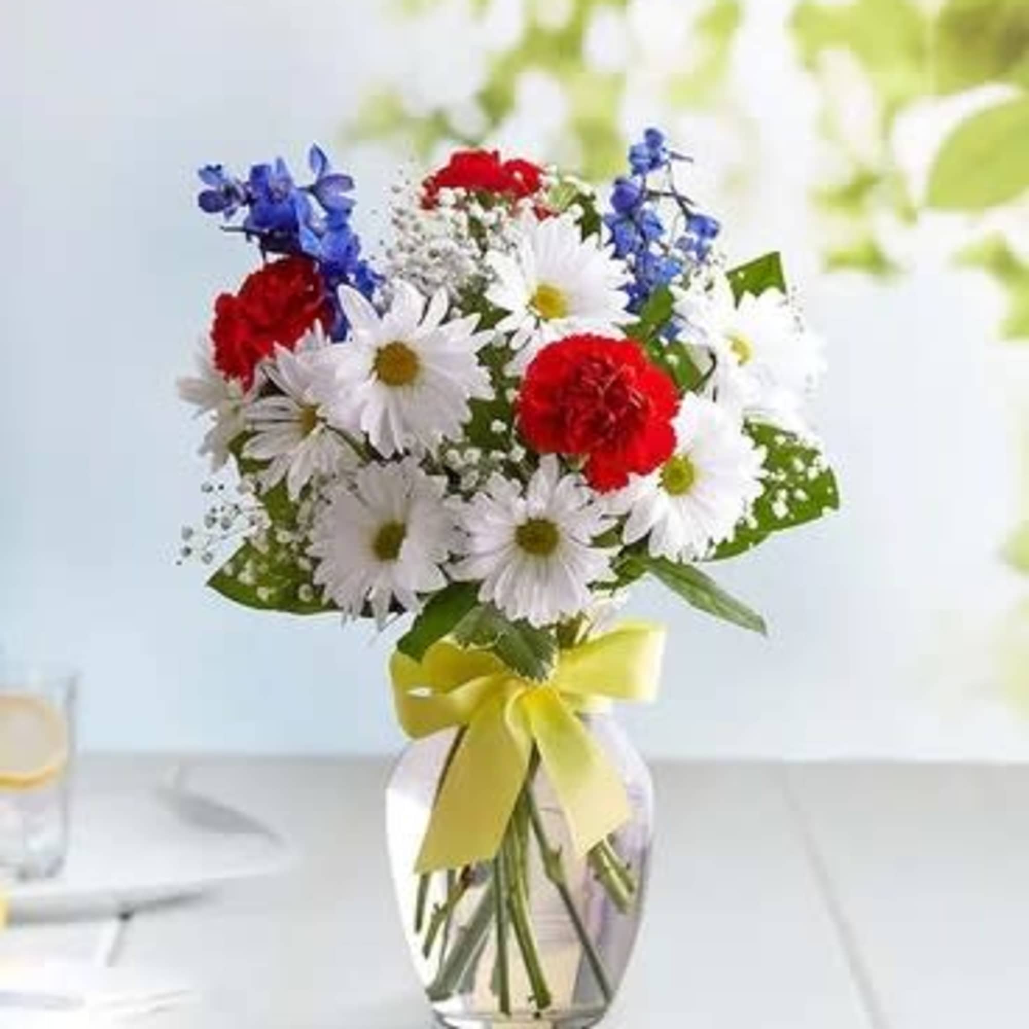 Bouquet of red, white, and blue flowers in a glass vase with a yellow ribbon