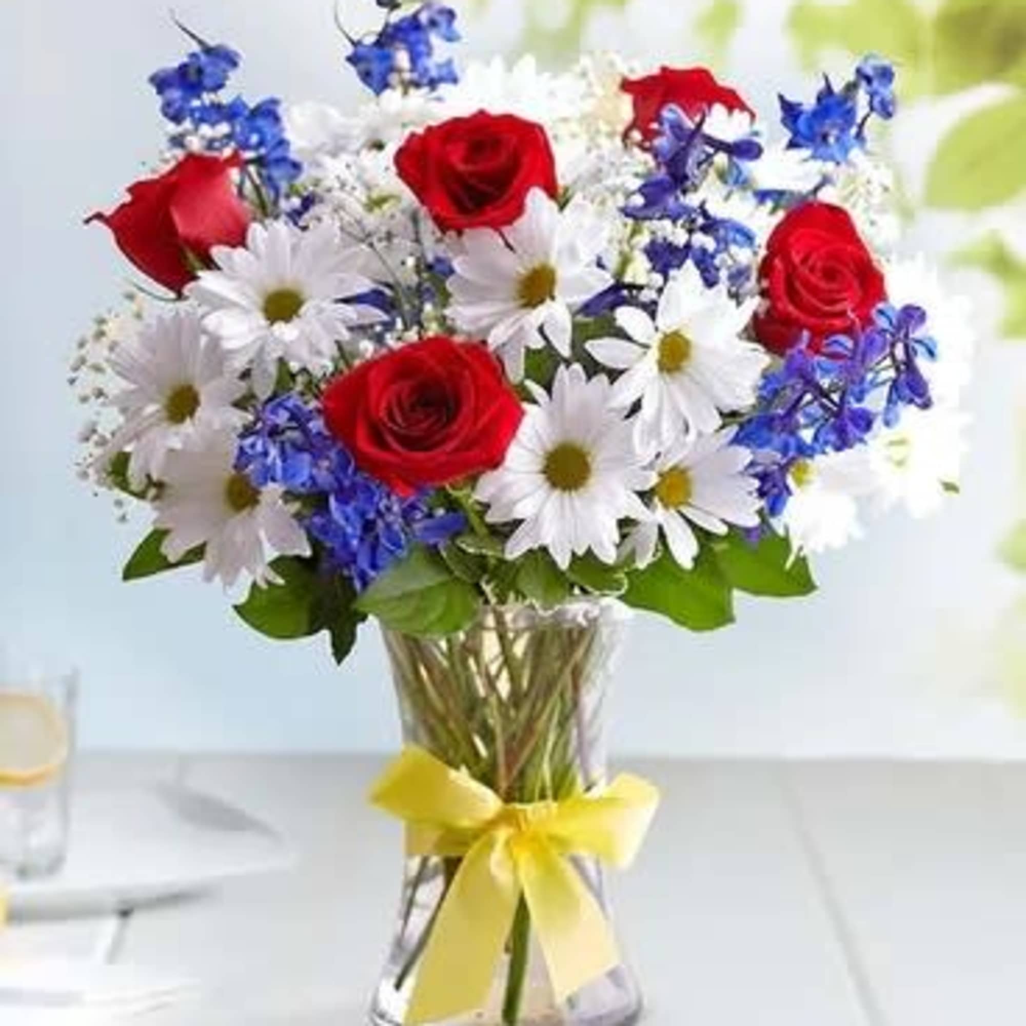 Bouquet of red roses, white daisies, and blue flowers in a glass vase