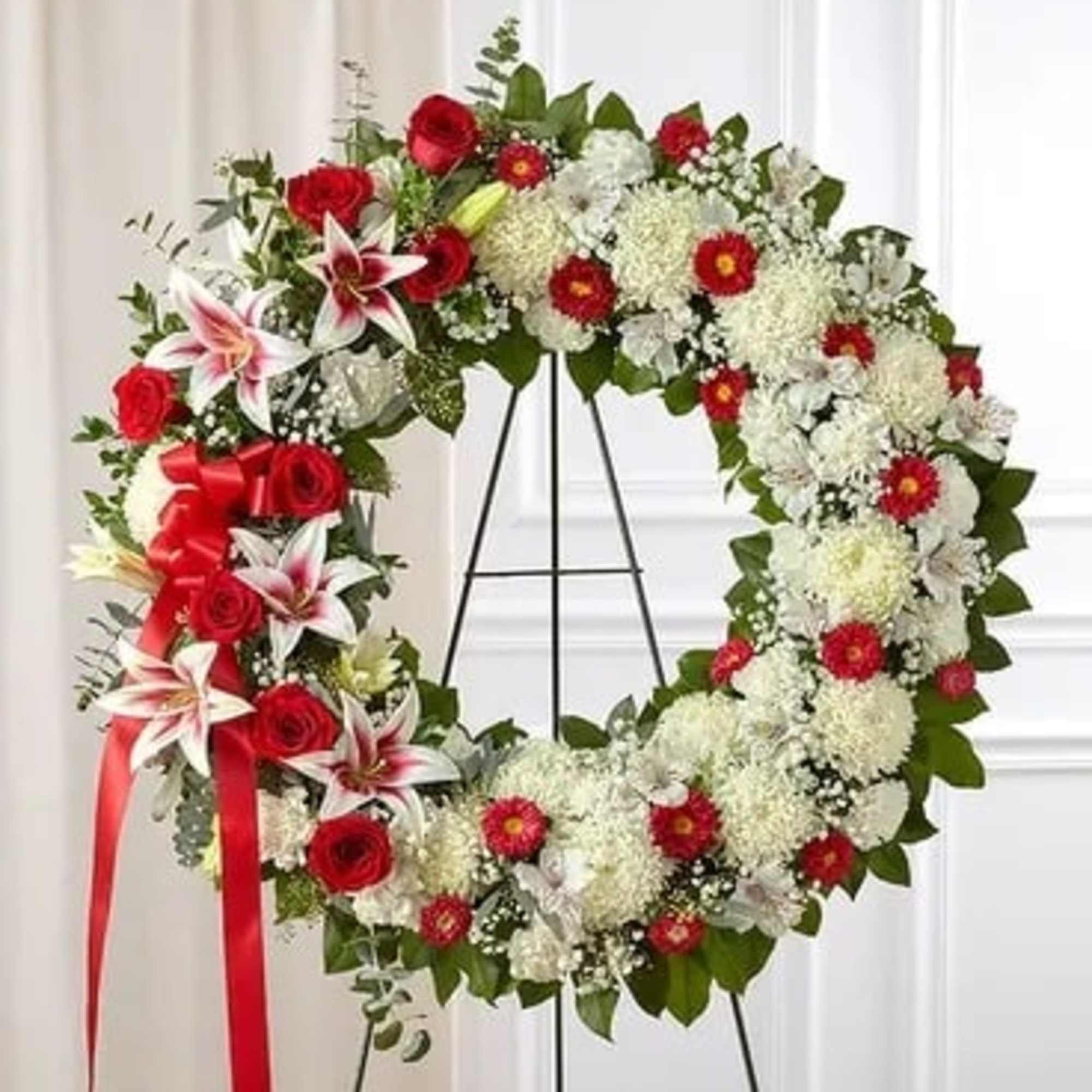Red and white floral wreath on a black stand with a red ribbon