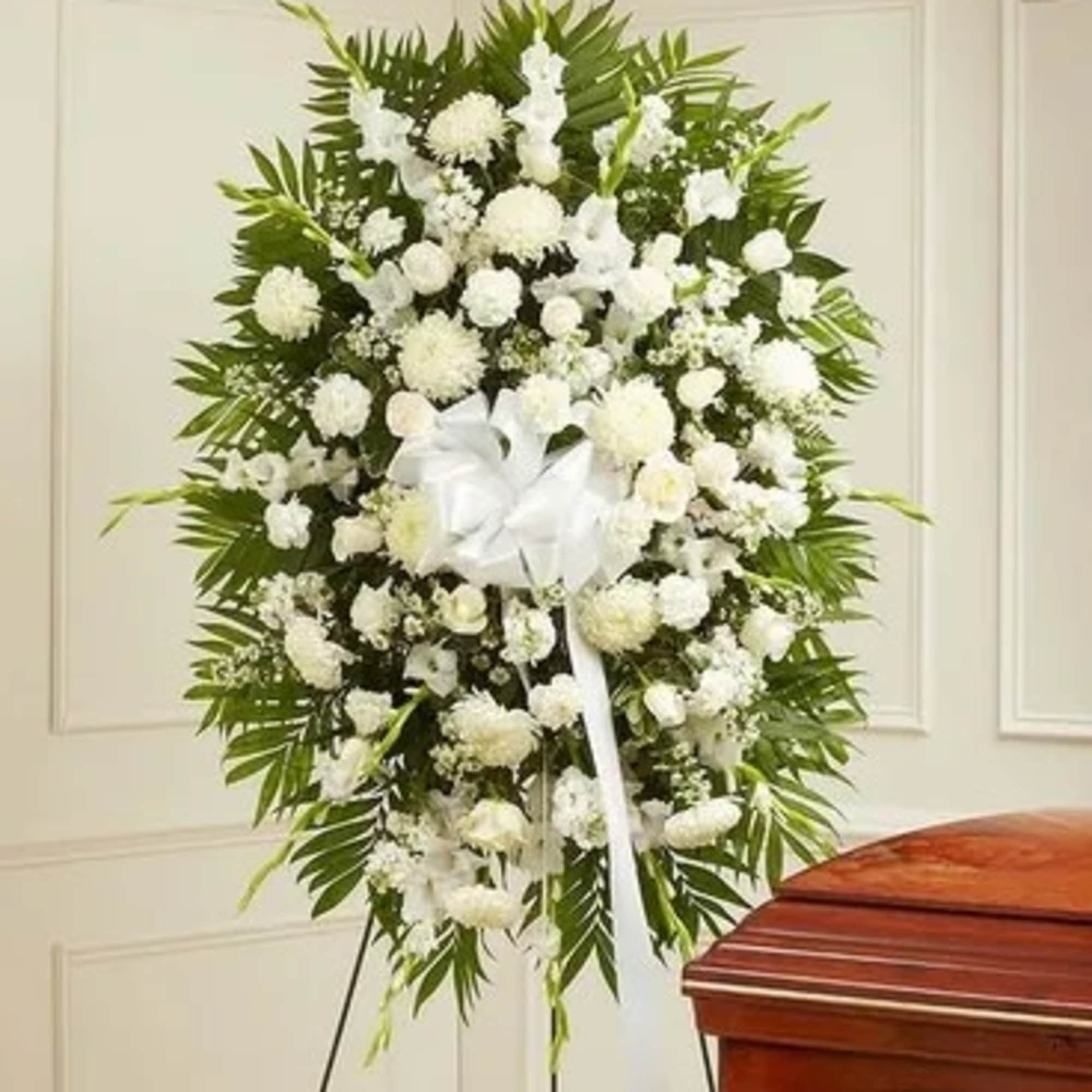 White funeral spray with a ribbon on an easel beside a casket