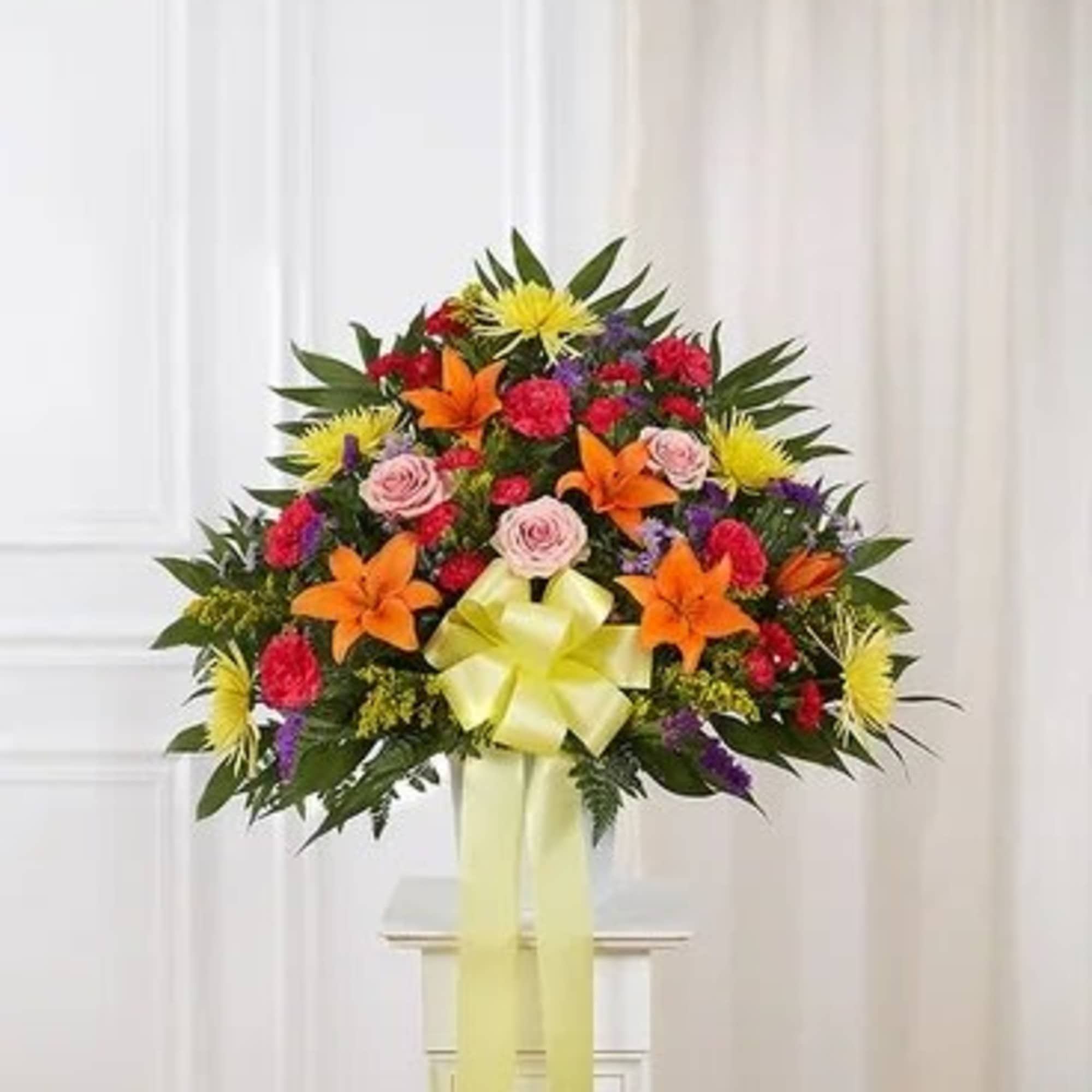Colorful standing floral spray with lilies, roses, and a yellow ribbon