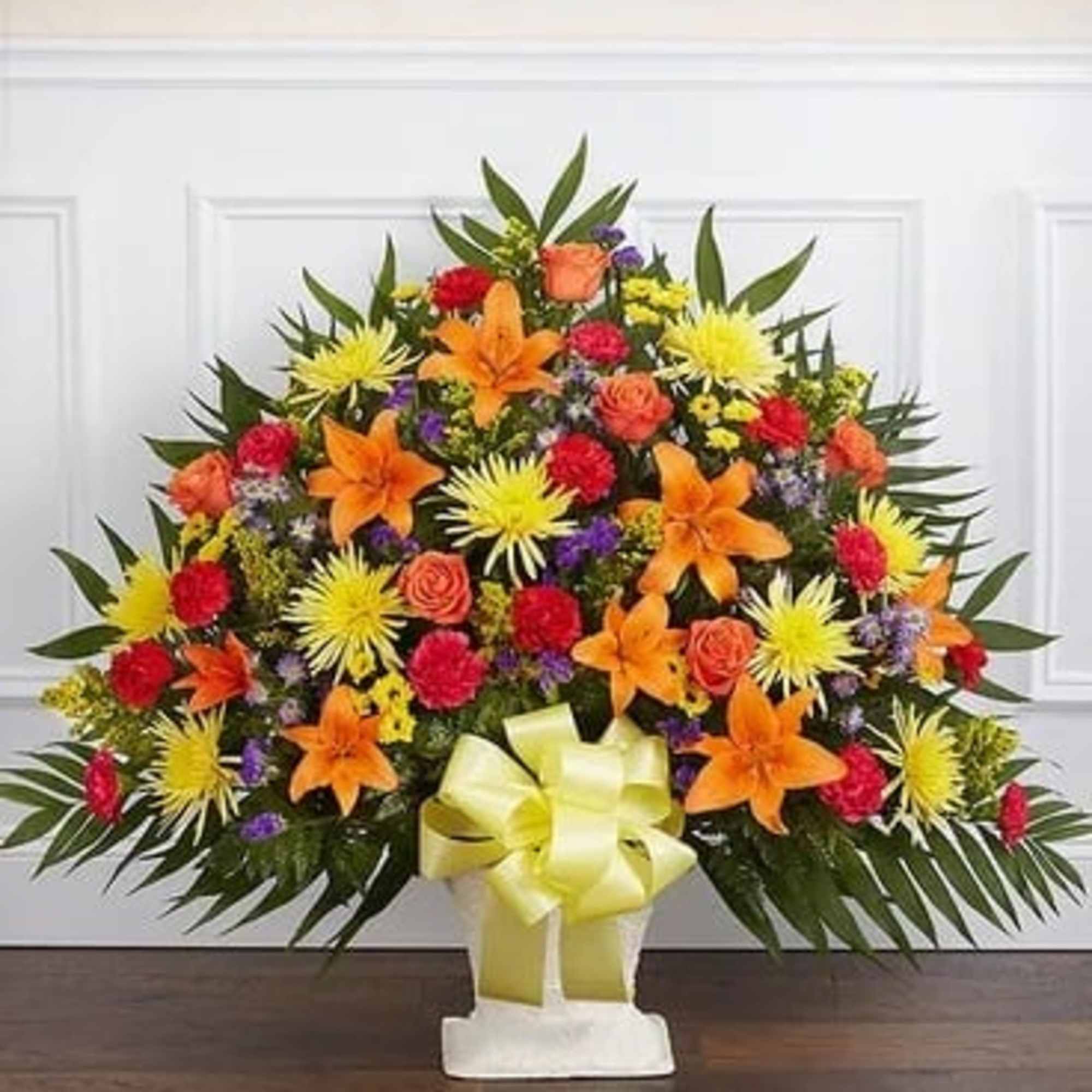 Bright mixed flower arrangement in a white pedestal vase with a yellow bow