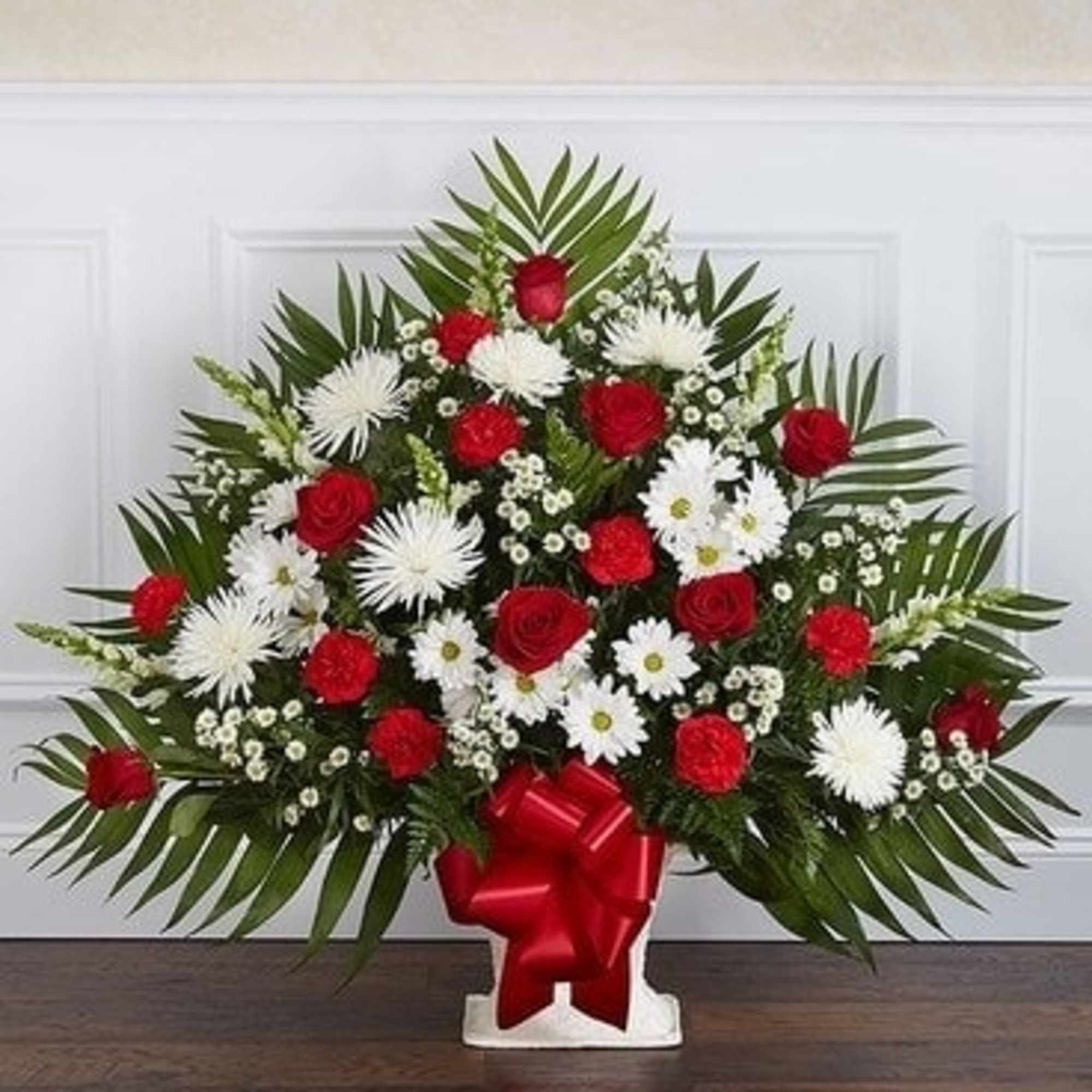 Red and white floral spray in a white vase with a red bow