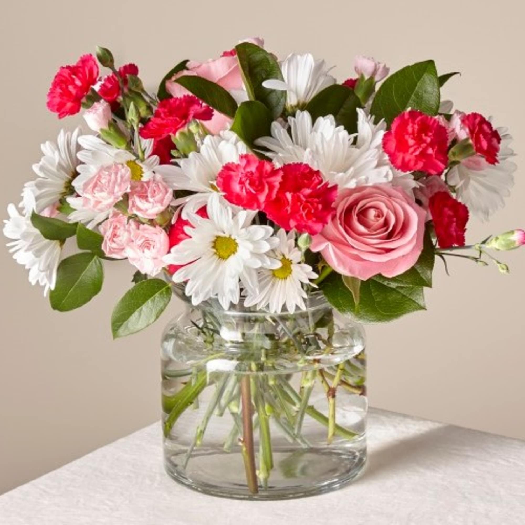Pink roses, carnations, and white daisies in a clear glass vase