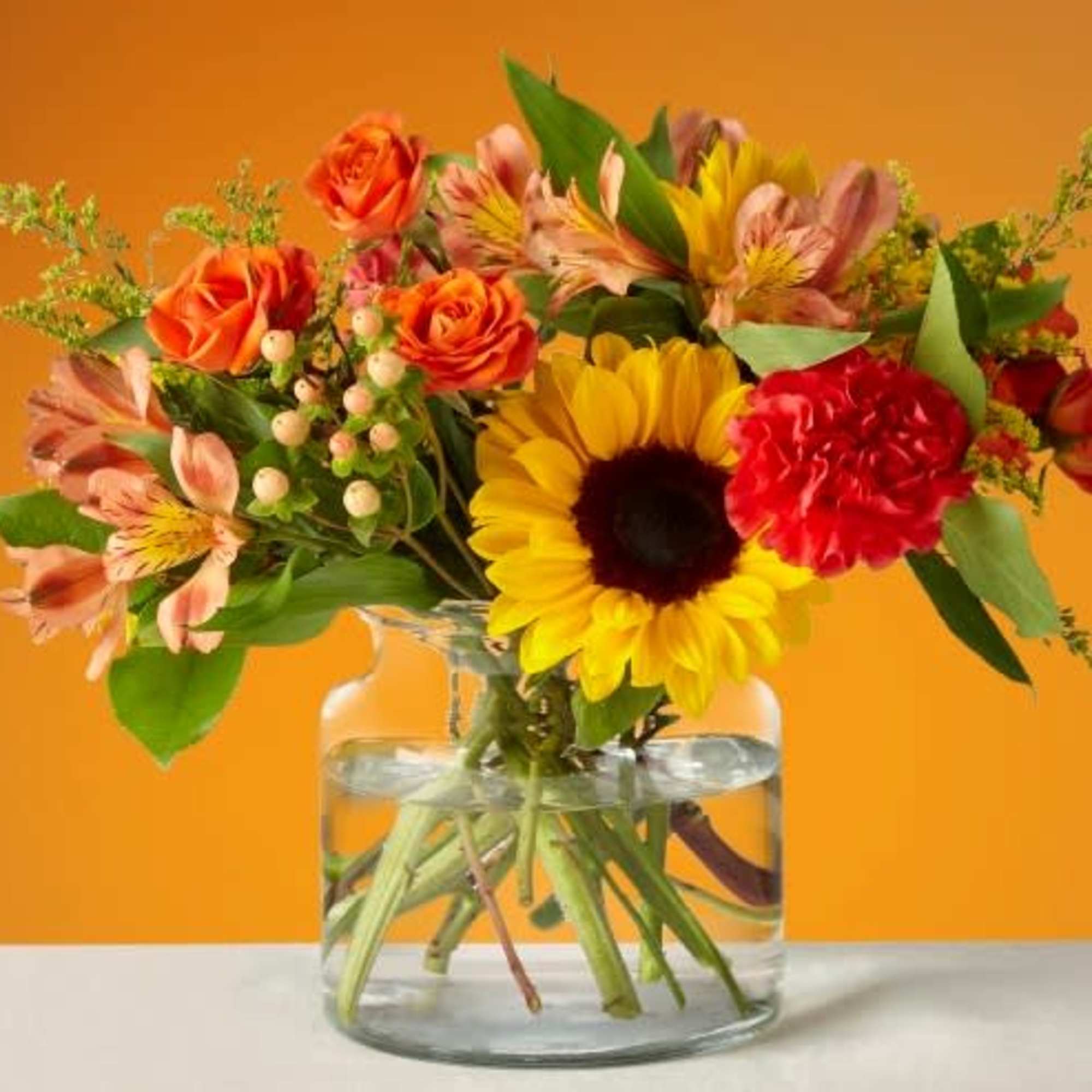 Mixed bouquet with sunflowers, orange roses, and red carnations in a glass vase