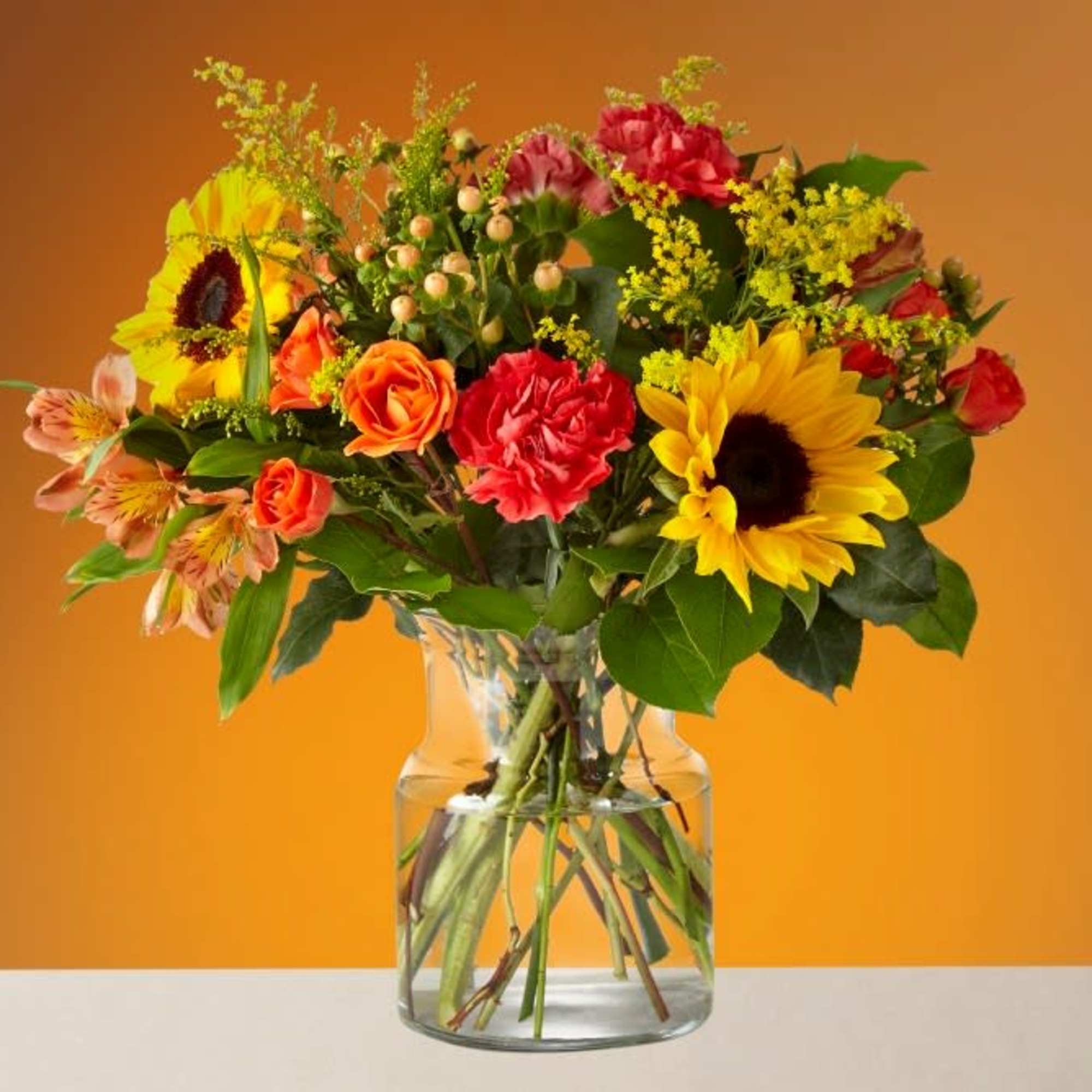Mixed bouquet of sunflowers, roses, and carnations in a clear glass vase