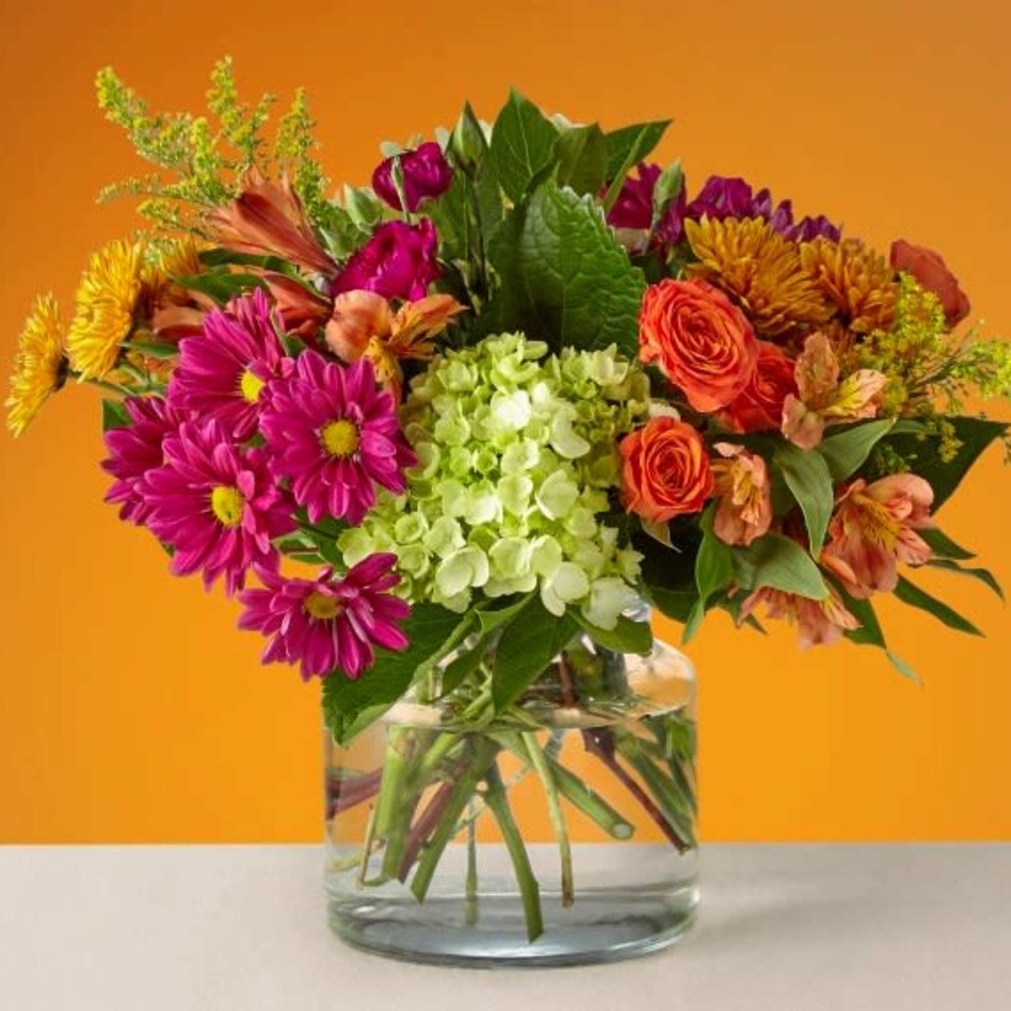 Mixed bouquet in a clear glass vase with pink, orange, yellow, and green blooms