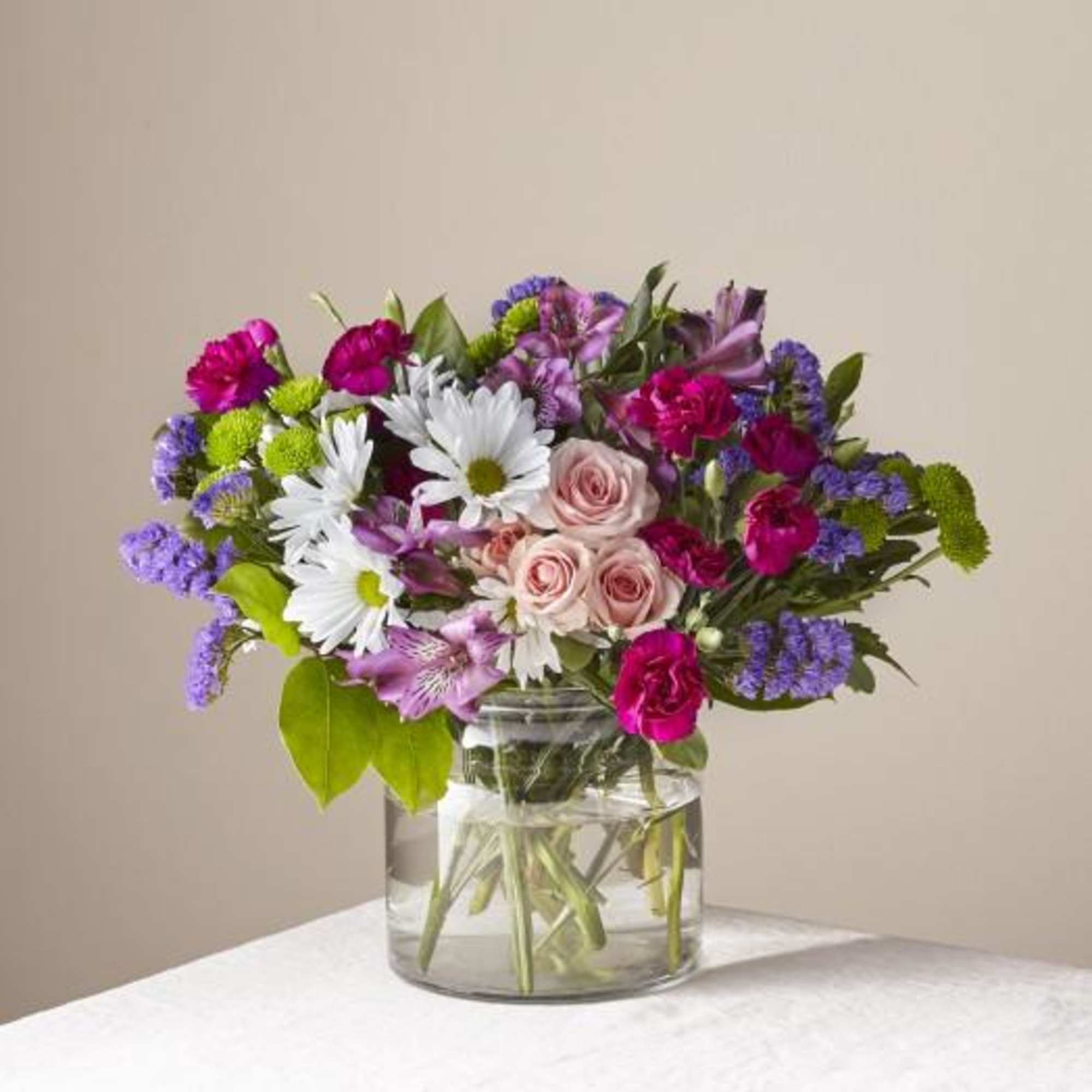 Mixed bouquet of pink roses, white daisies, and purple flowers in a glass vase
