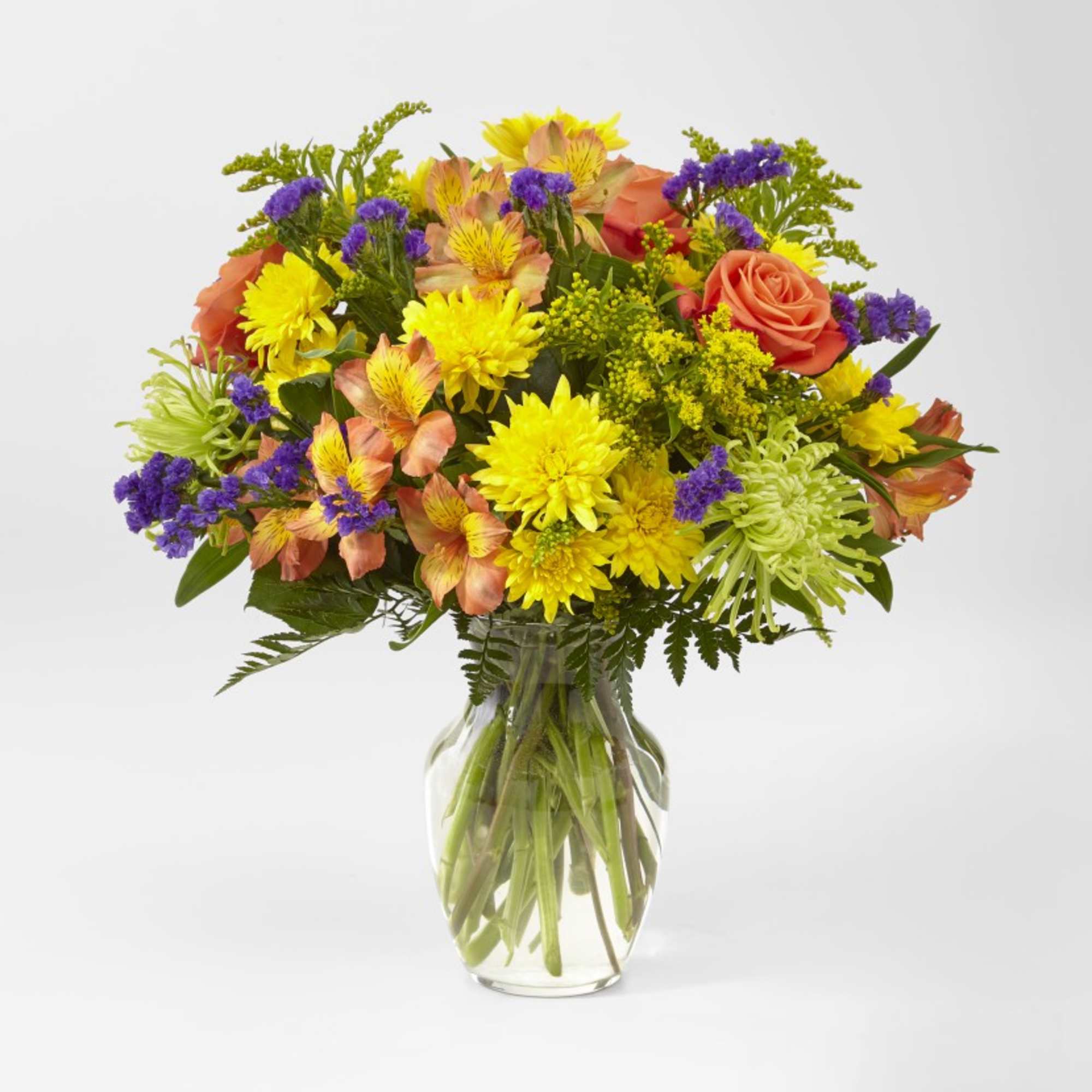 Mixed bouquet of yellow, orange, and purple flowers in a clear glass vase