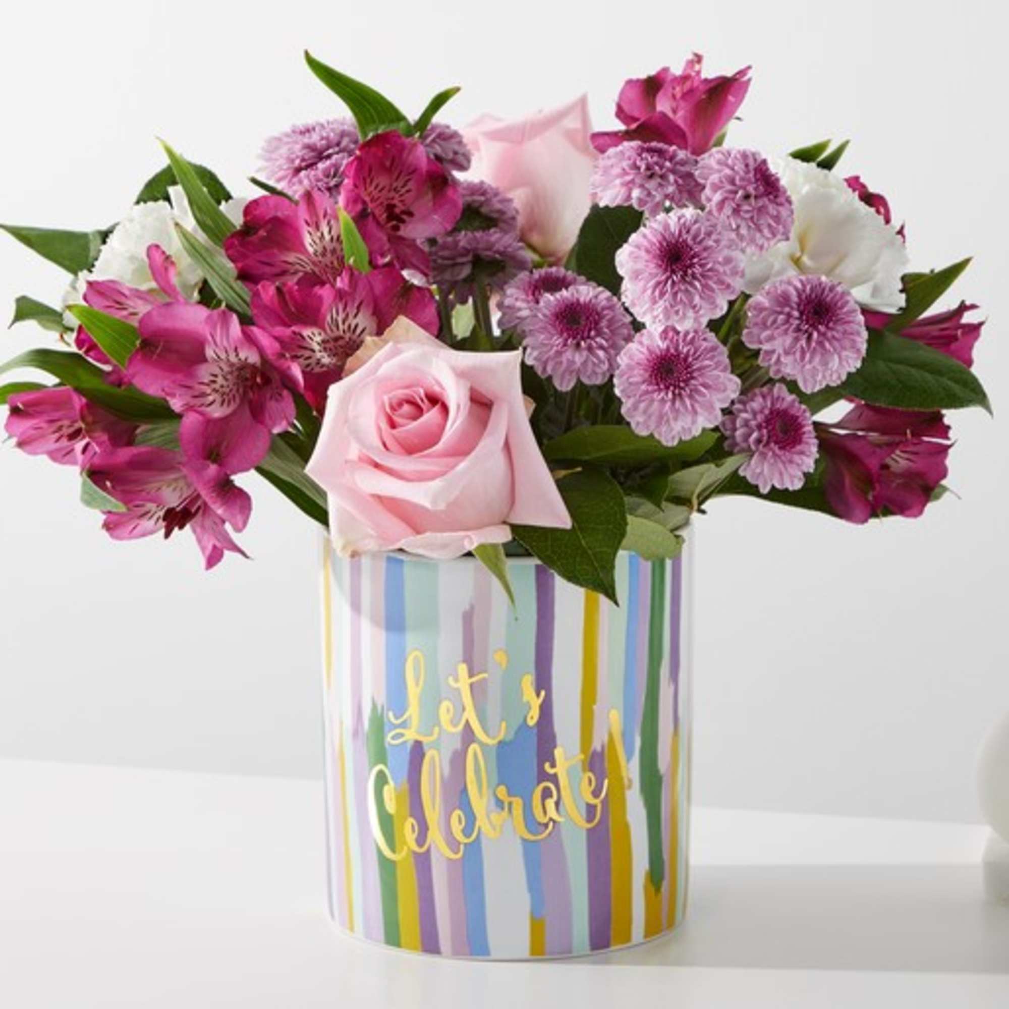Pink and purple mixed bouquet in a striped vase with "Let's Celebrate" text