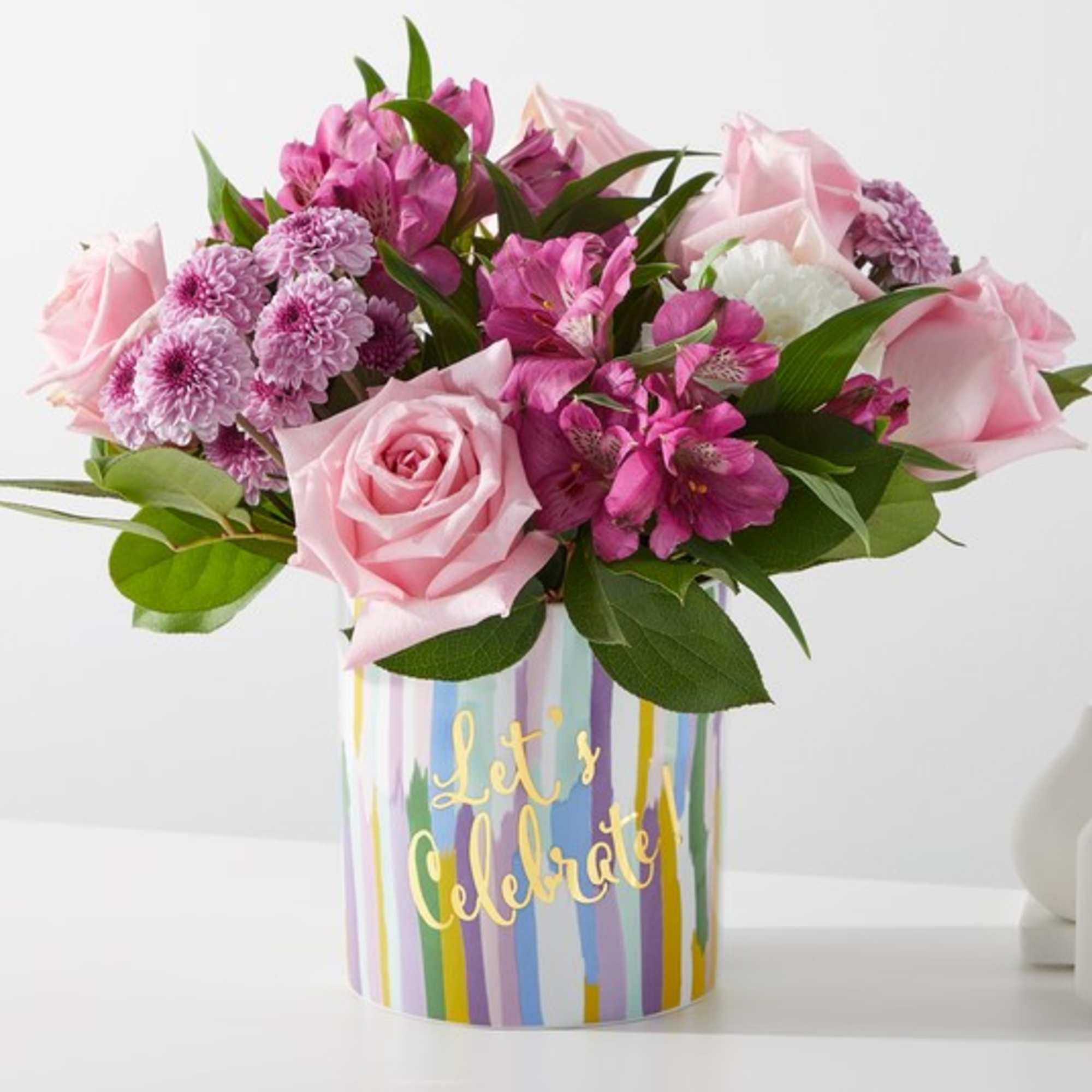 Pink roses and purple flowers in a striped vase with "Let's Celebrate" text