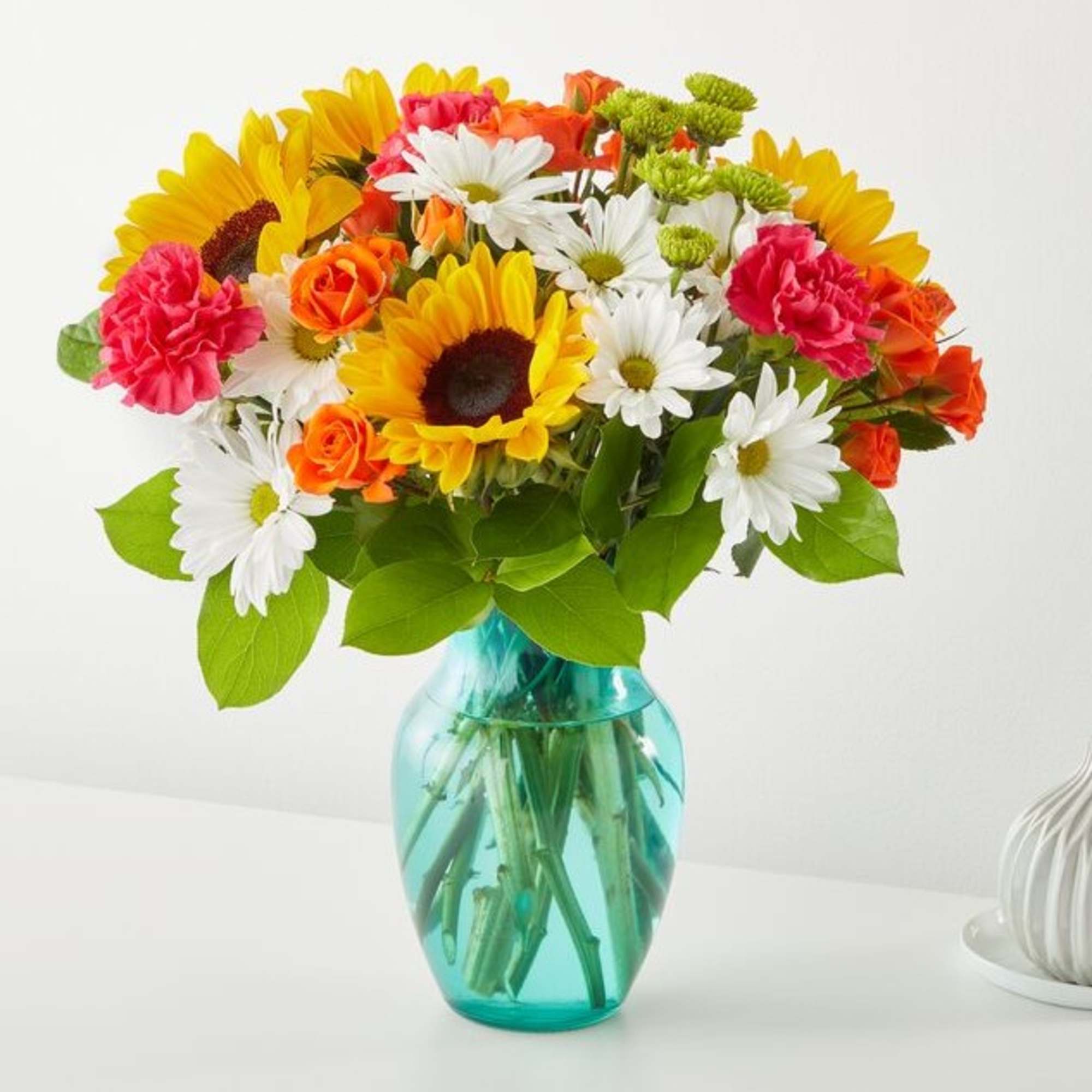 Mixed bouquet of sunflowers, daisies, roses, and carnations in a blue glass vase