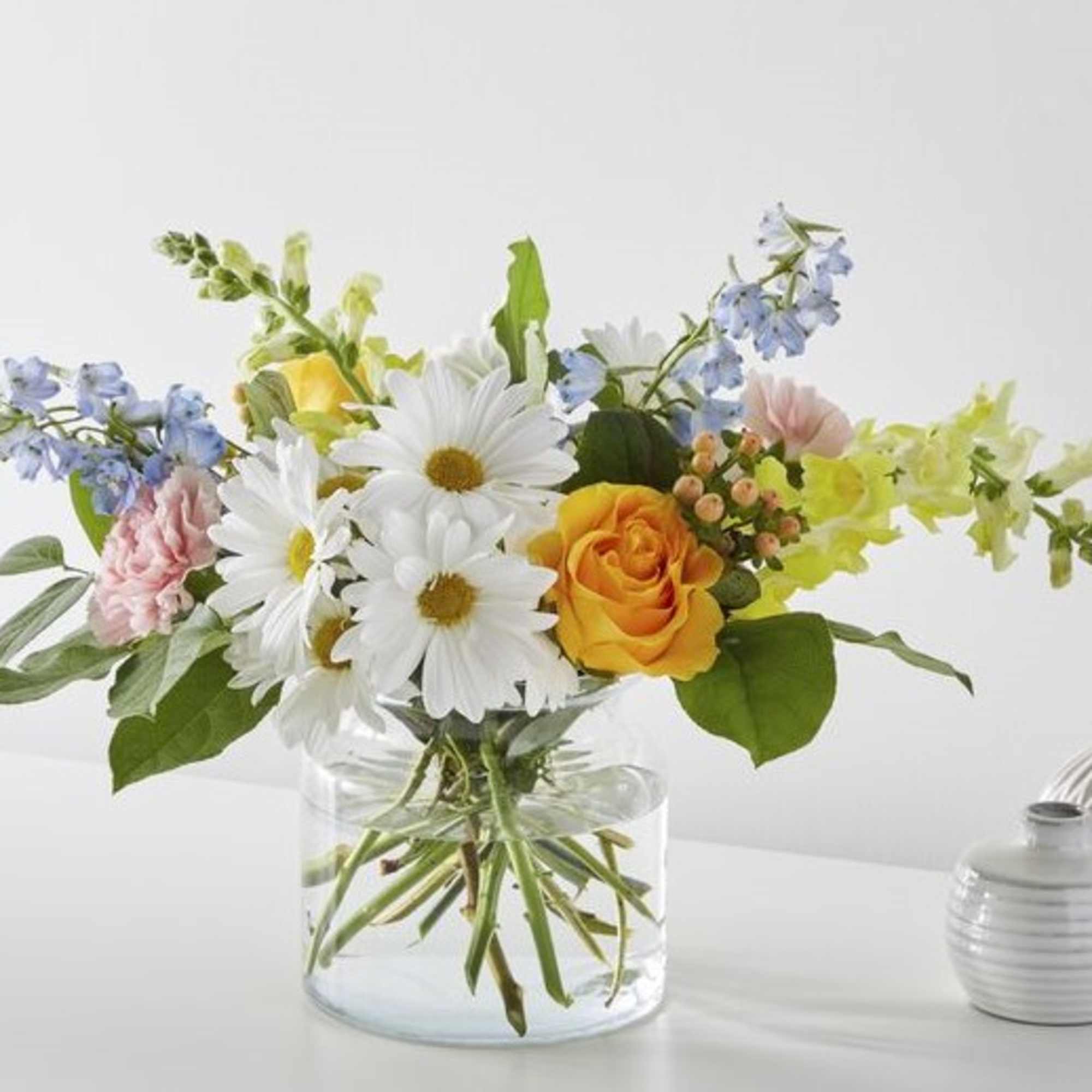 Bouquet of daisies, roses, and blue flowers in a clear glass vase