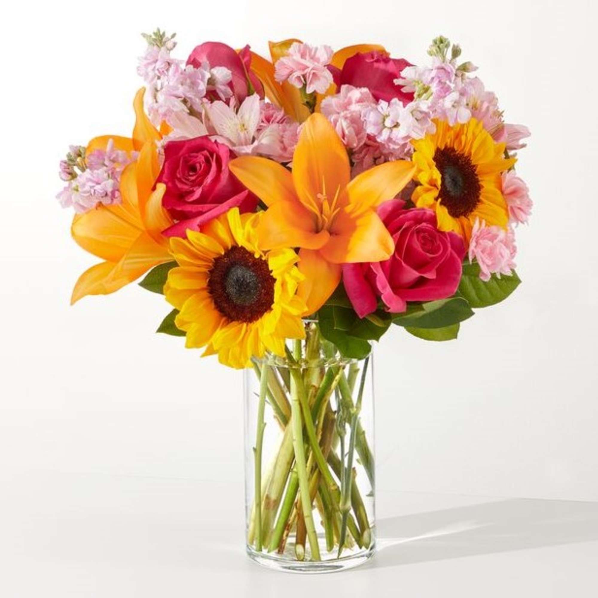 Bouquet of pink roses, orange lilies, and sunflowers in a clear glass vase