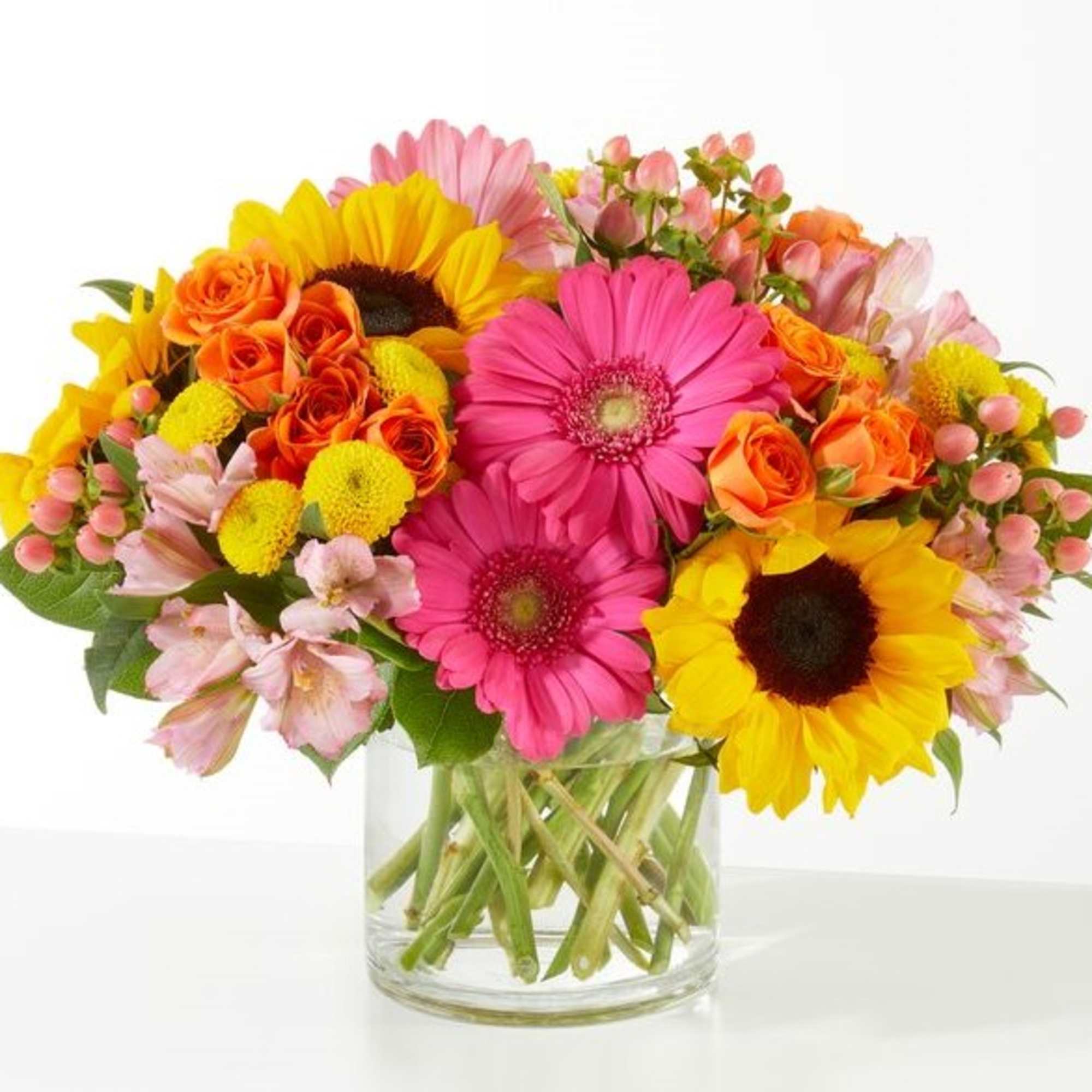 Mixed bouquet of sunflowers, gerbera daisies, and orange roses in a glass vase