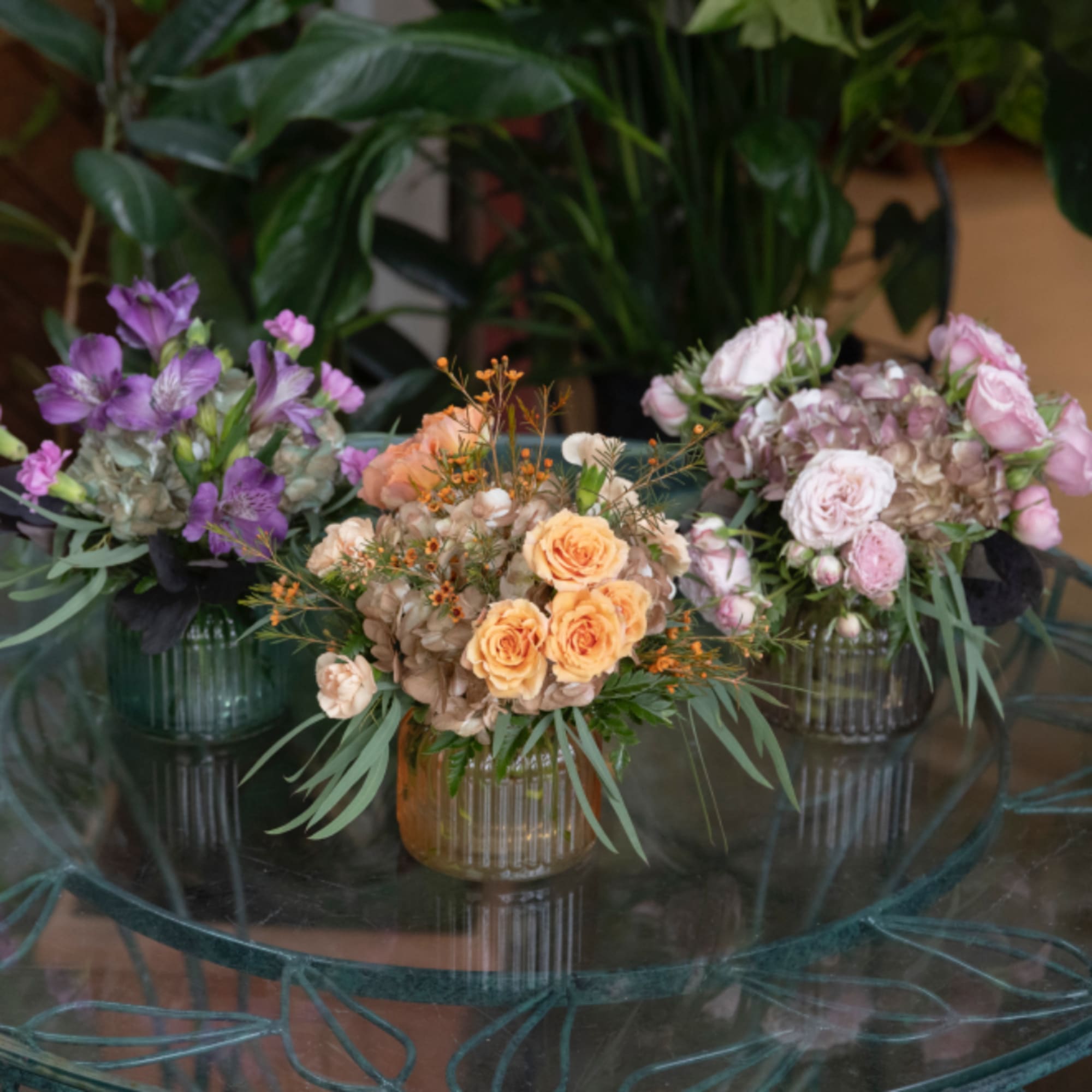 Three small floral arrangements in ribbed glass vases on a table, photo 2 of 3