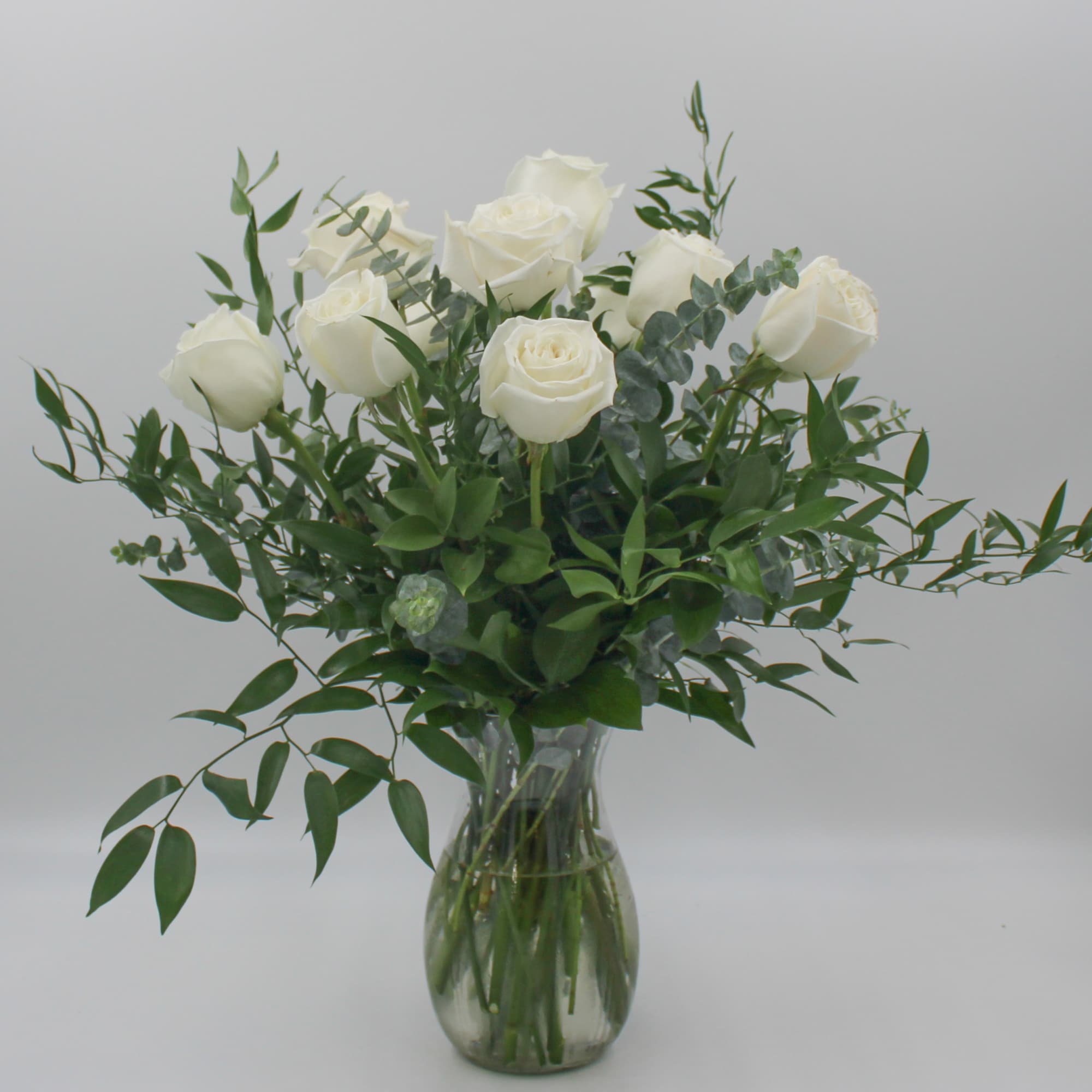 White roses in a clear glass vase with greenery