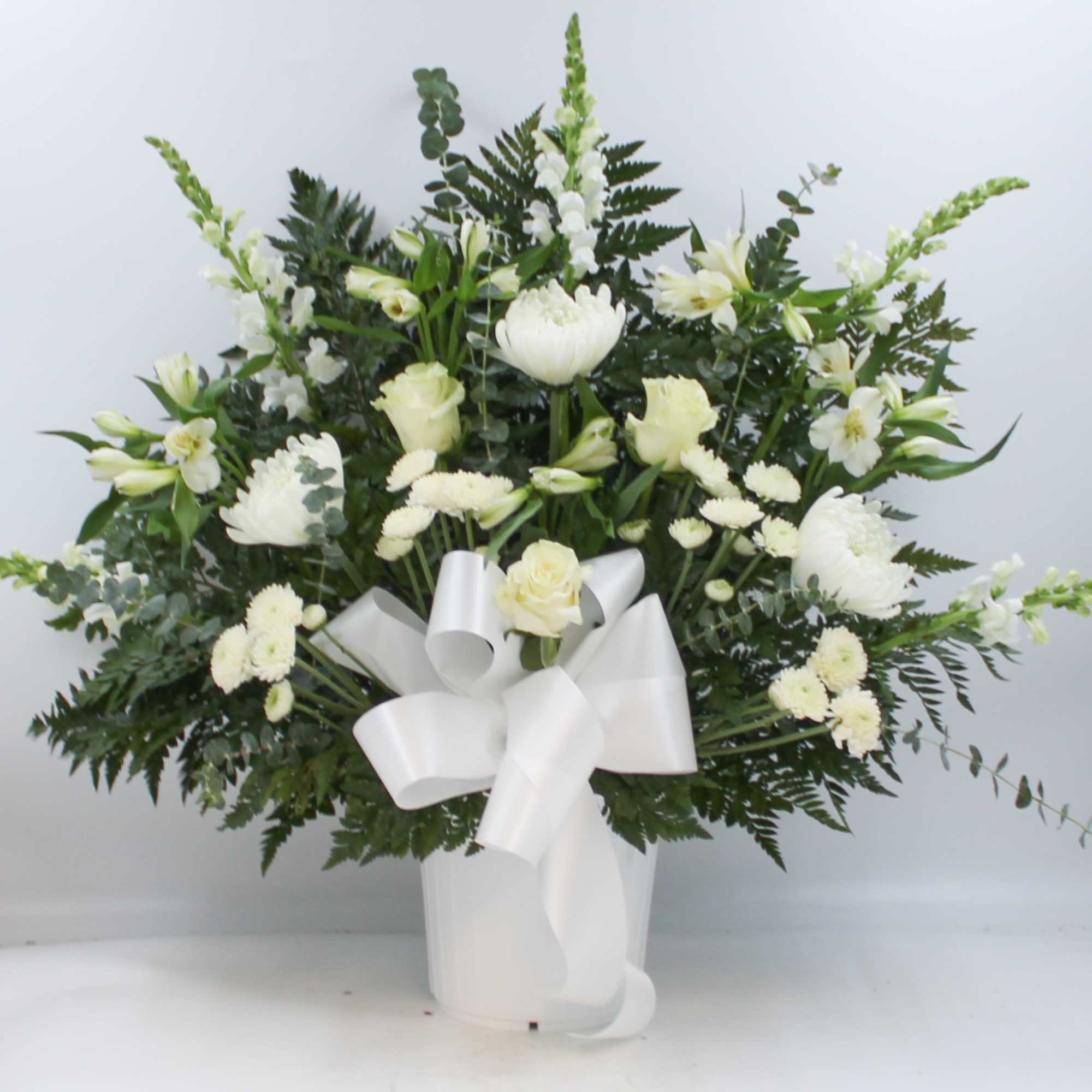 White floral arrangement in a white vase with a large ribbon bow
