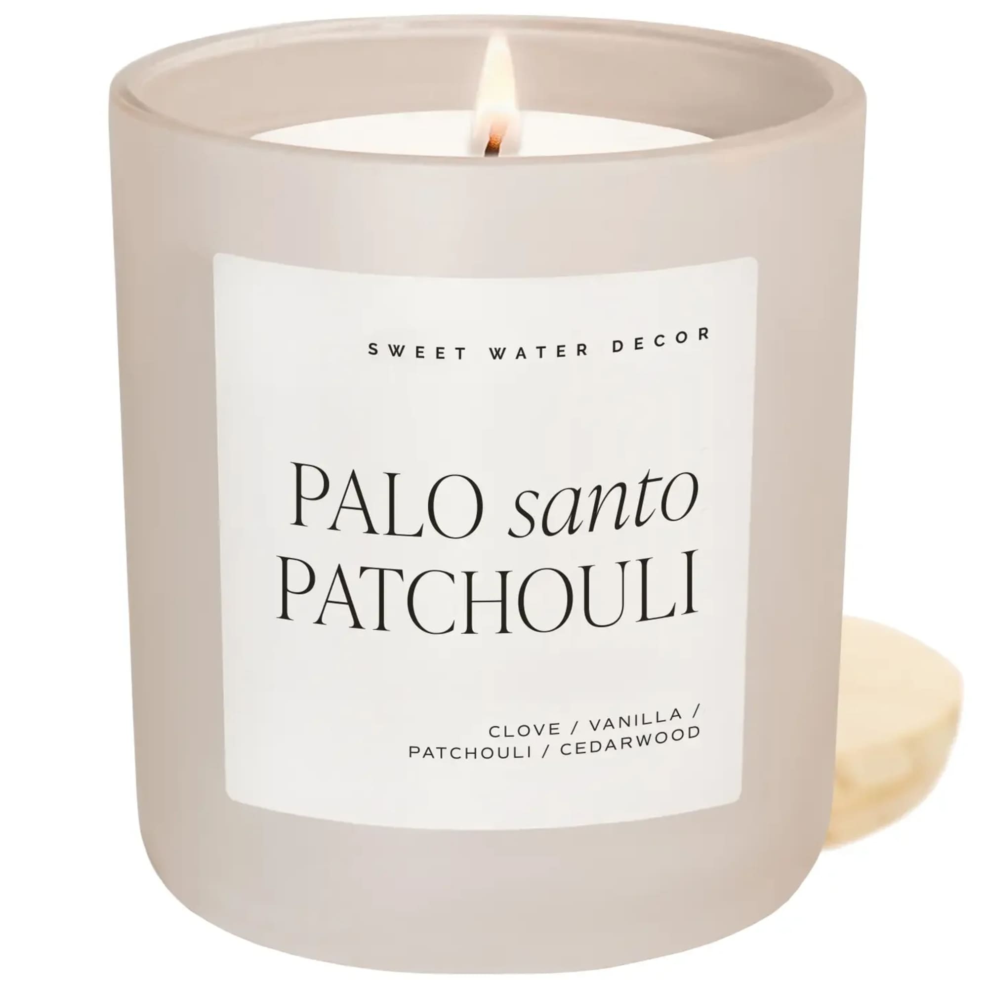 Lit beige candle in a glass jar with a white label