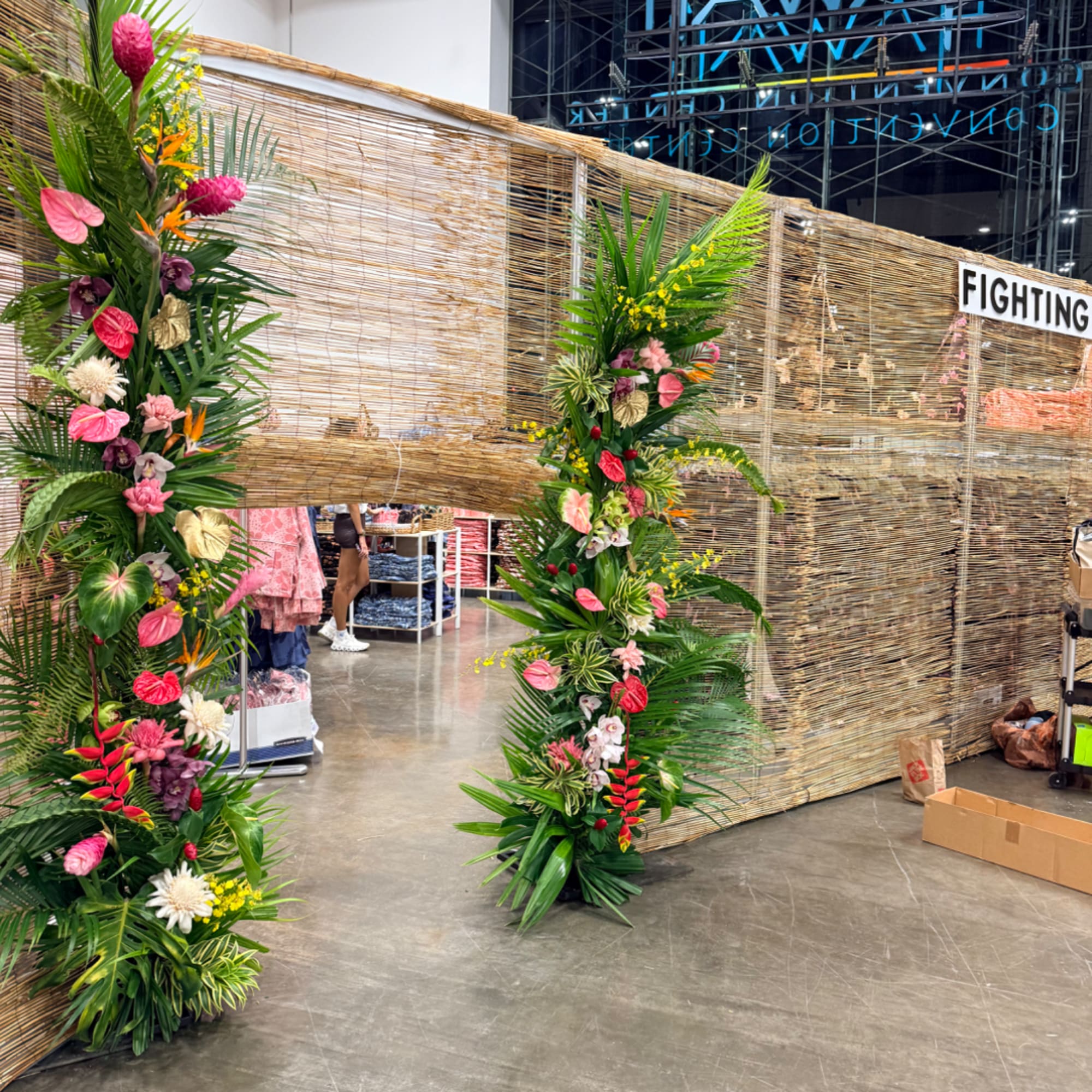 Two tall tropical floral columns with pink and yellow blooms beside a woven wall.