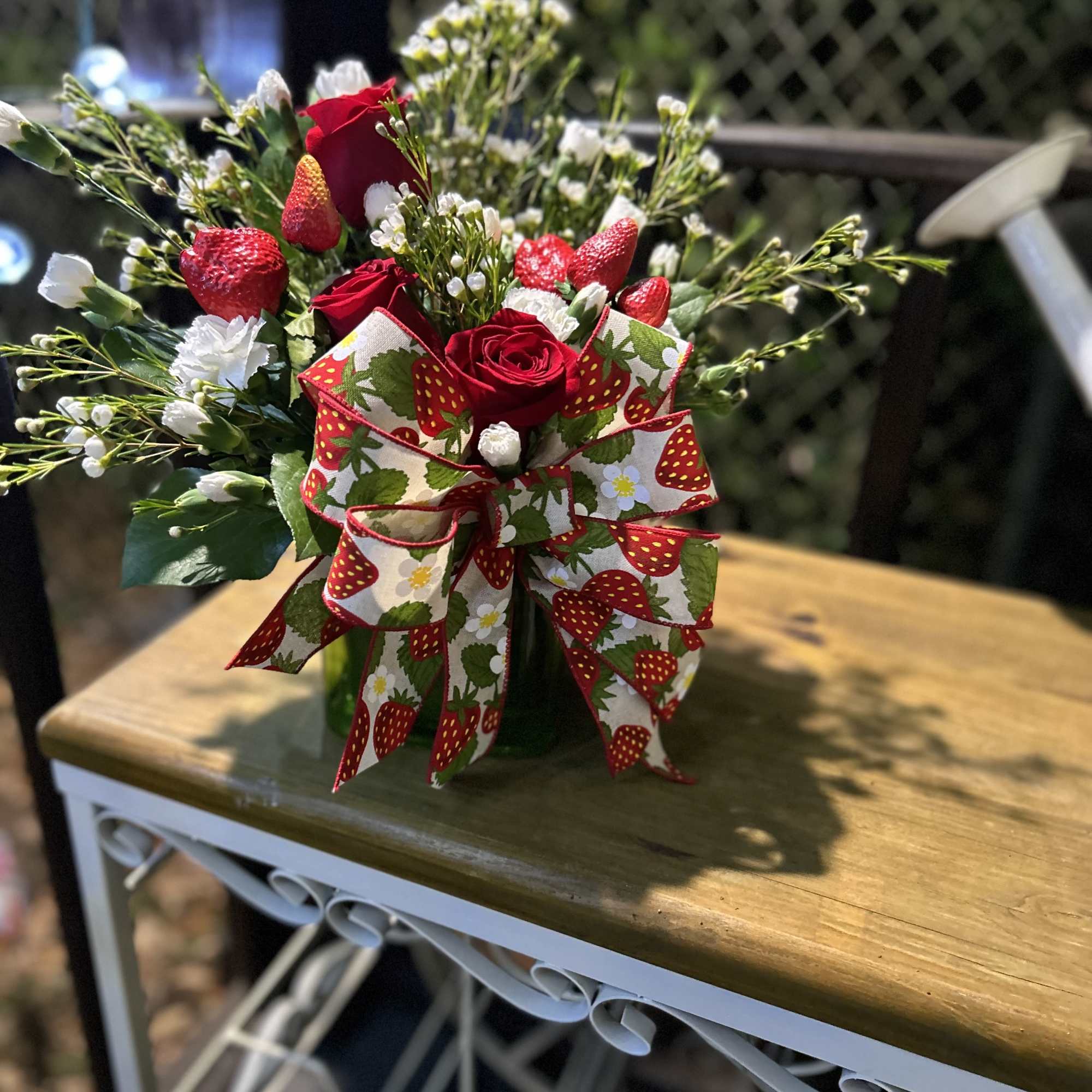 Arrangement of red roses and white flowers with strawberries and a strawberry-print bow in a vase