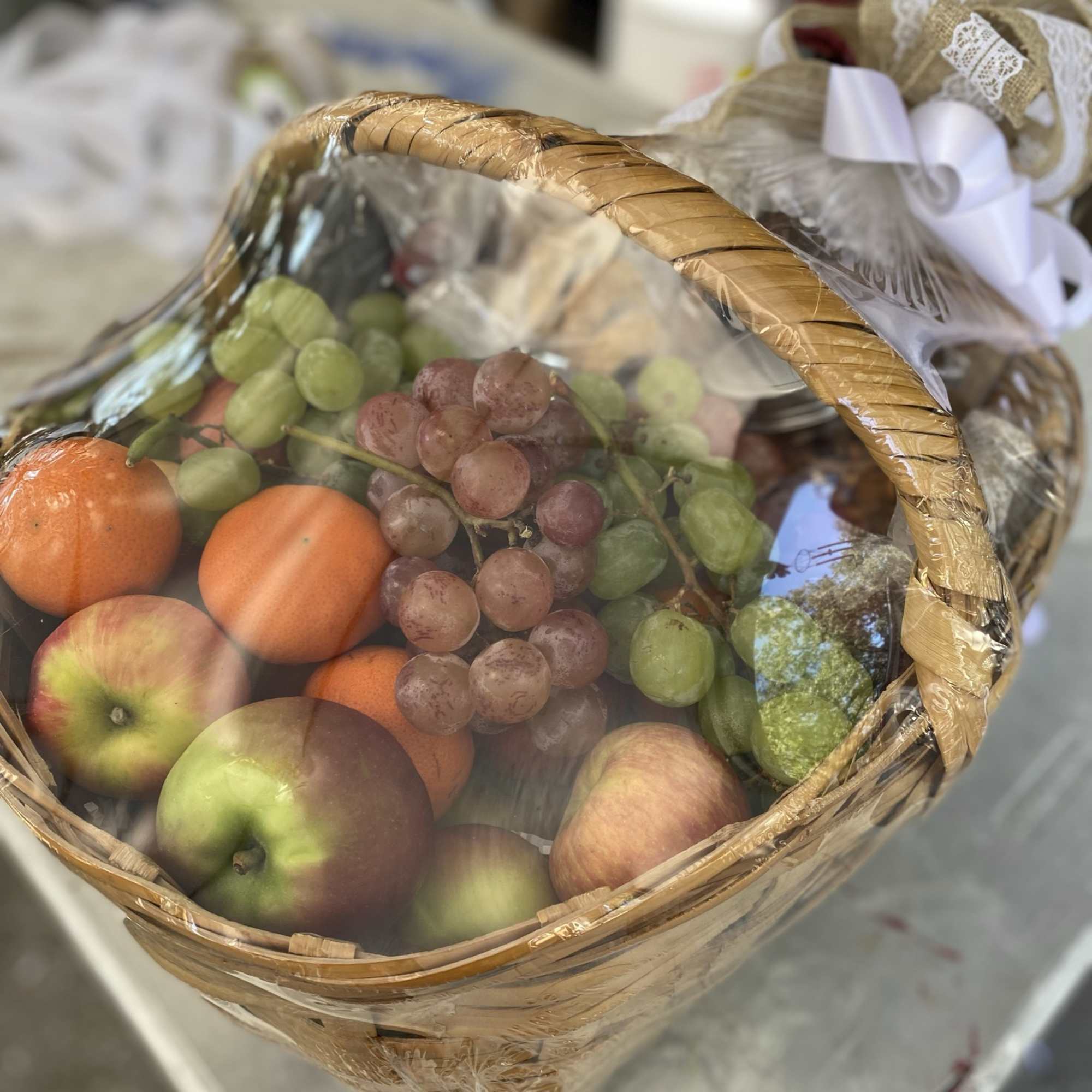 Gift basket of apples, oranges, and grapes wrapped in cellophane with a decorative bow