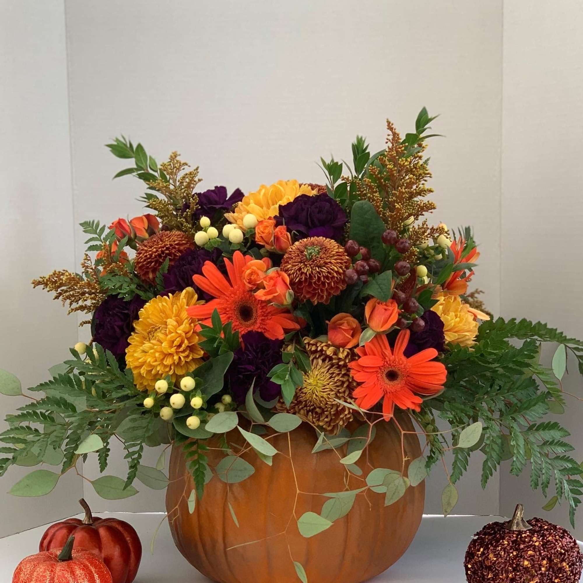 Autumn arrangement of orange and yellow flowers in a pumpkin container with small decorative pumpkins nearby