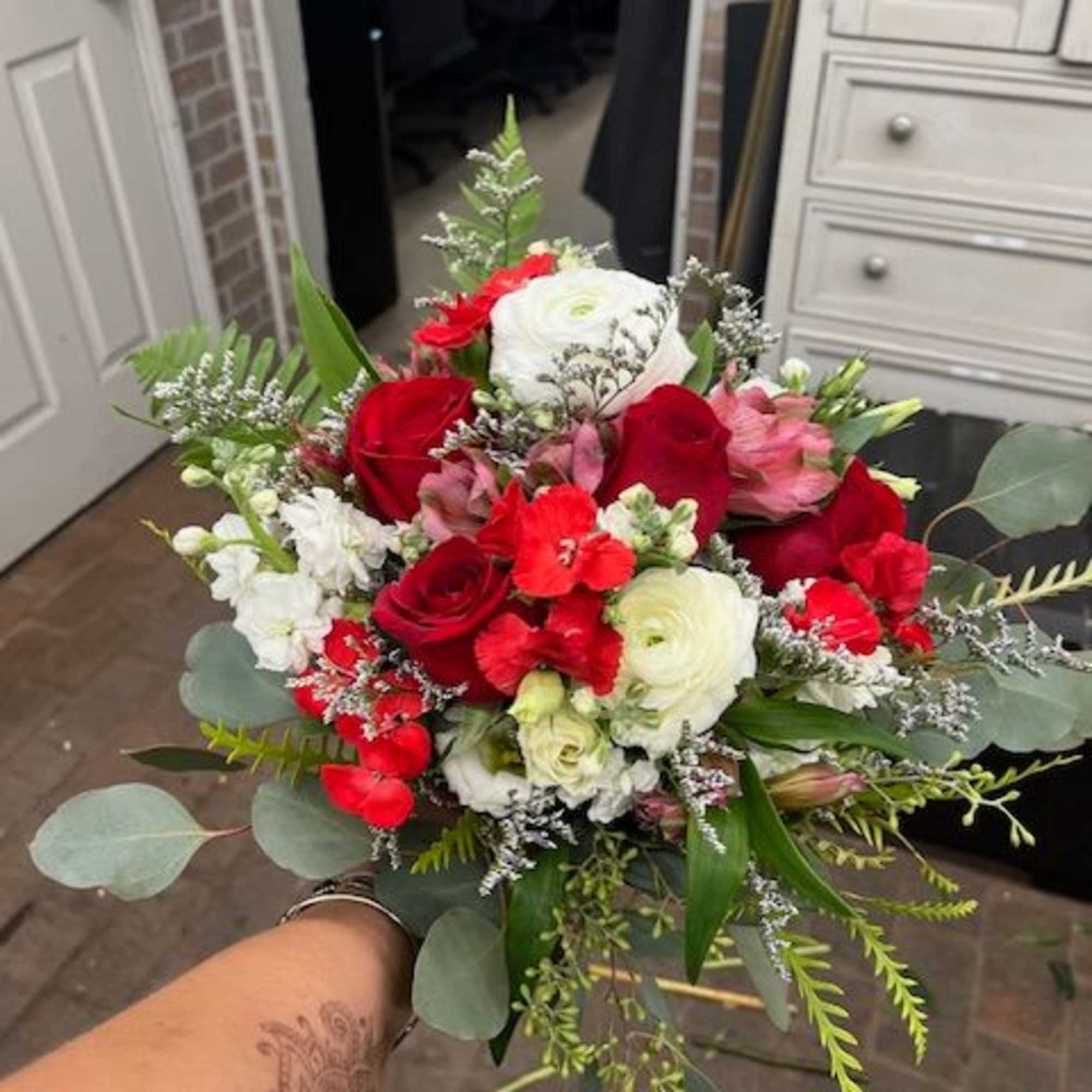 Handheld bouquet of red, white, and pink flowers with greenery