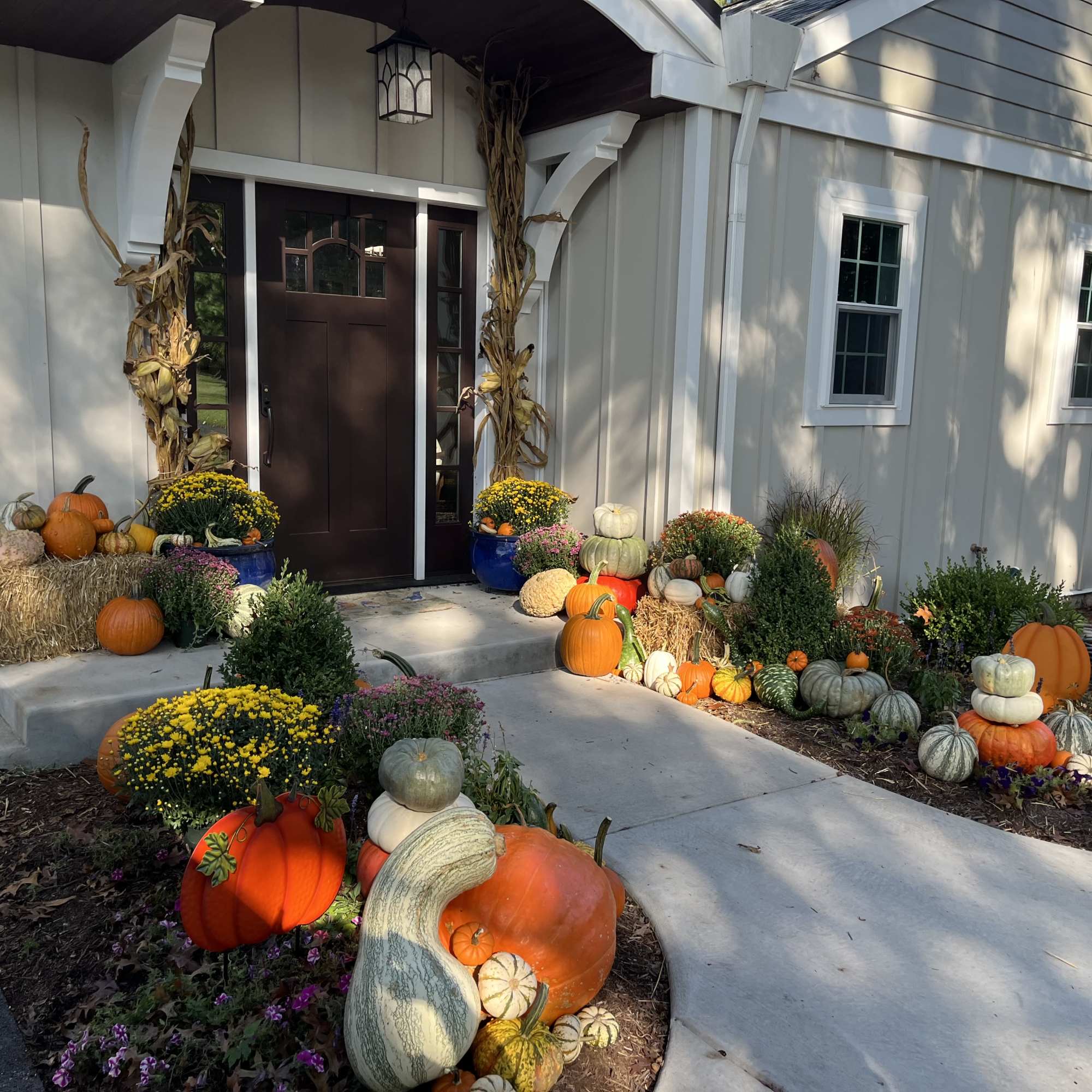 Front porch decorated with pumpkins, hay bales, and potted mums