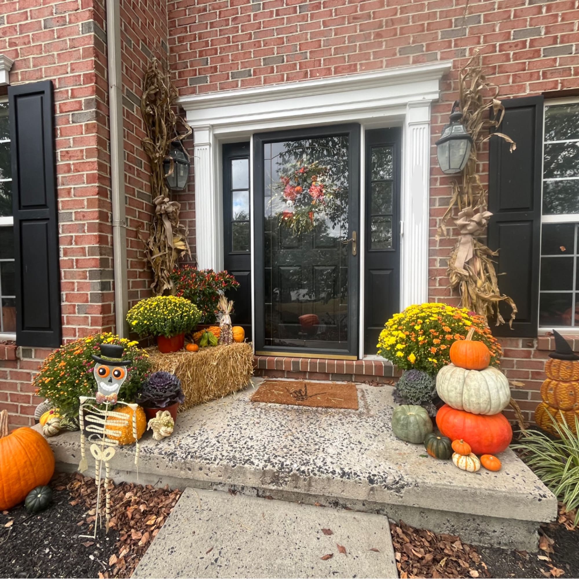 Fall porch display with mums, pumpkins, hay bales, and a skeleton decoration