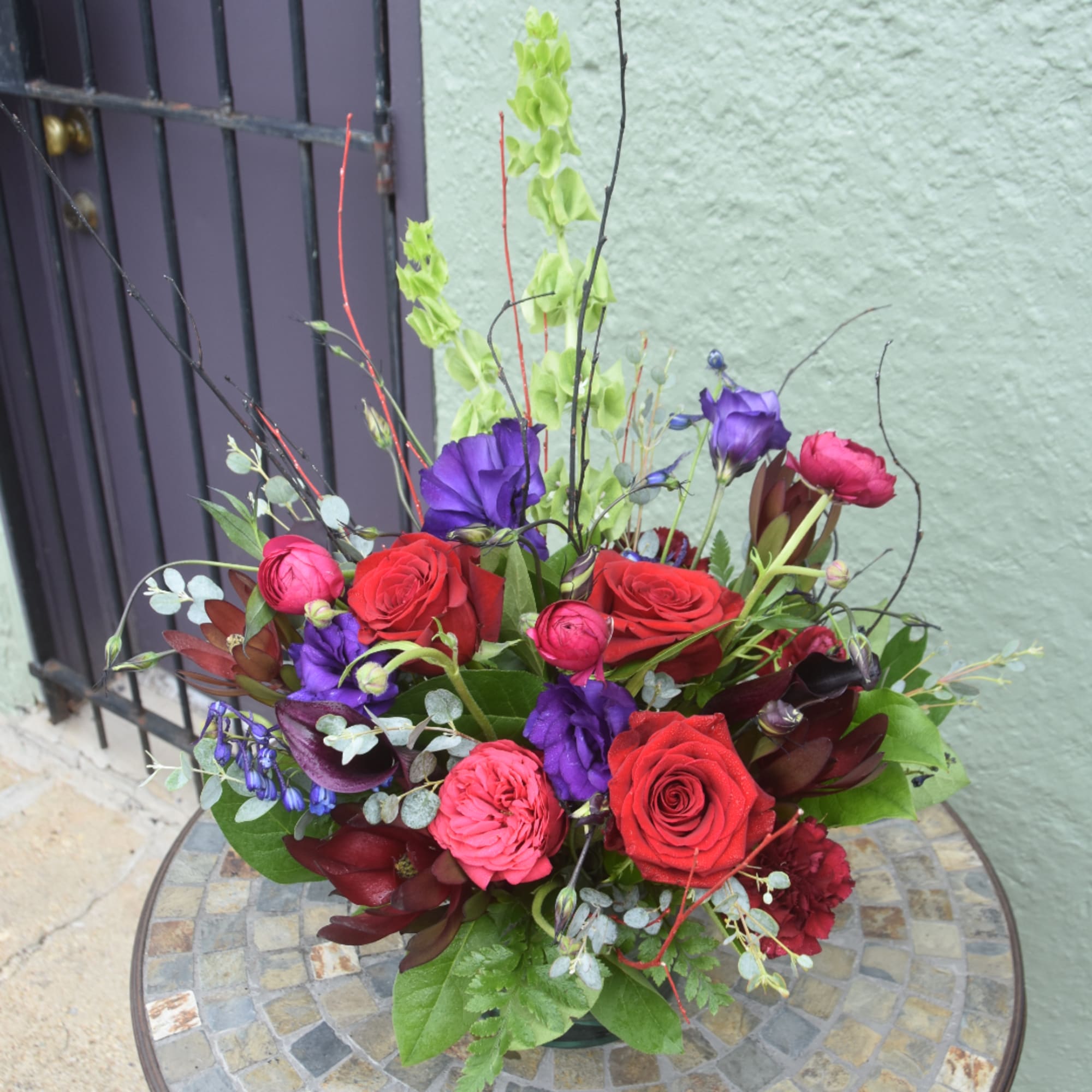 Mixed bouquet of red and pink roses with purple blooms in a low container